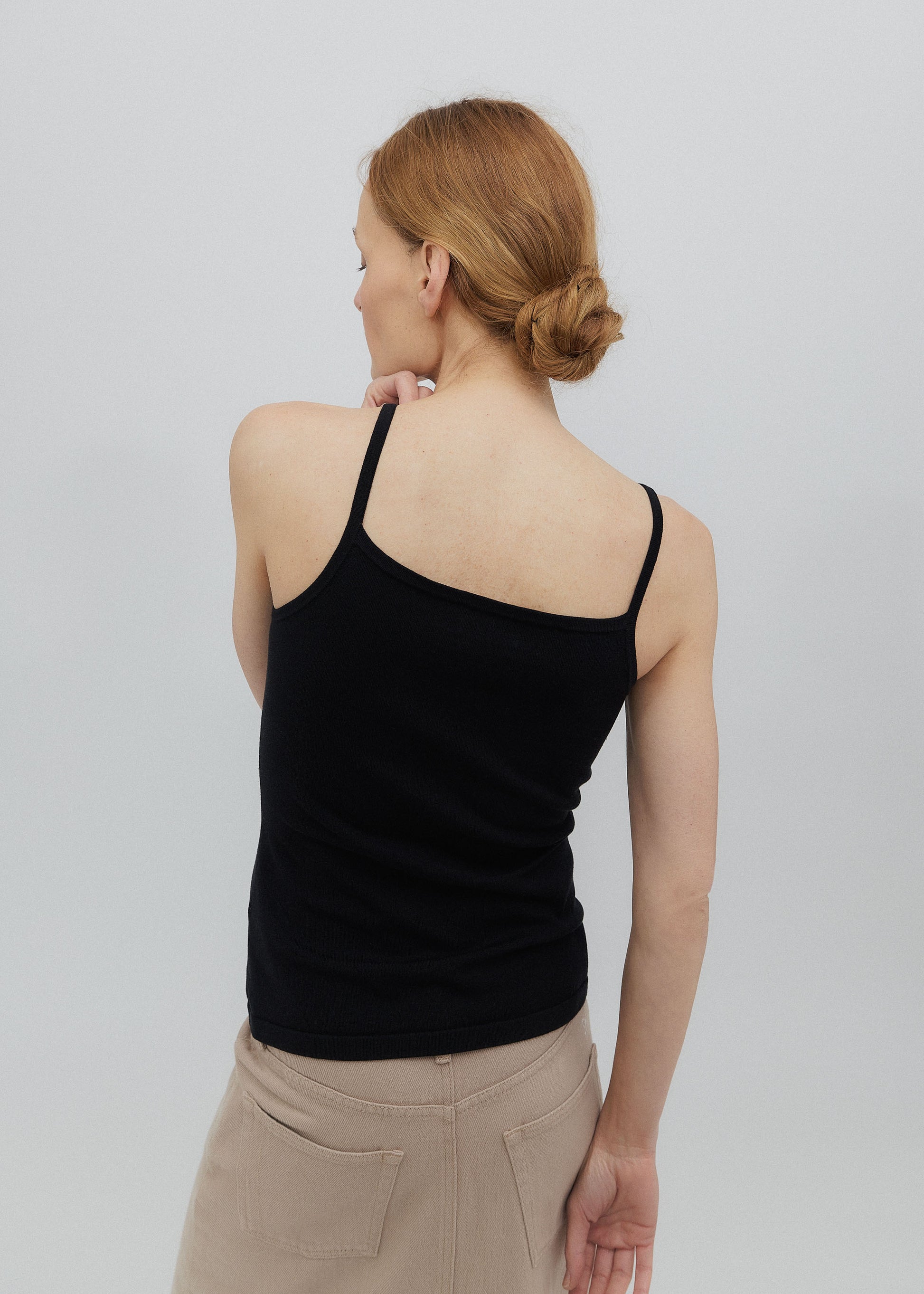 Woman wearing a black tank top and beige pants against a plain background