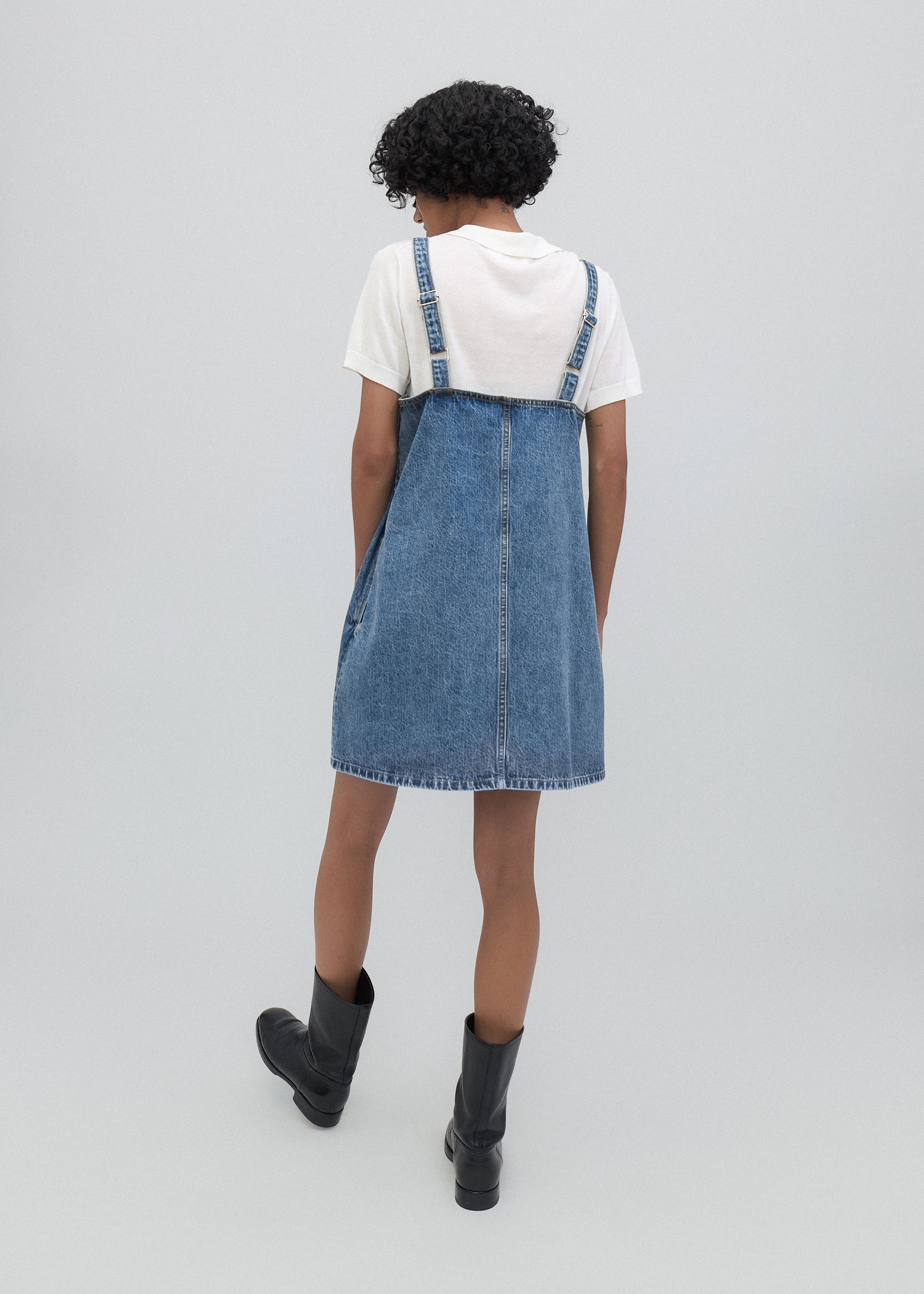 Person wearing a denim pinafore dress on a plain background