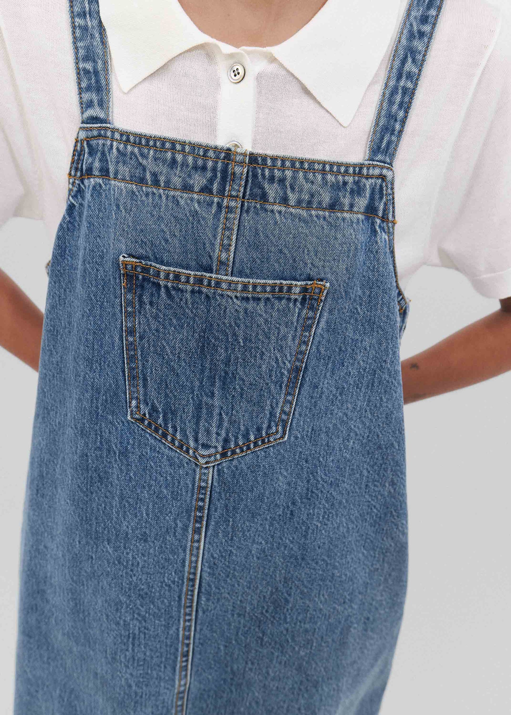 Person wearing a white shirt and blue denim overalls on a plain background
