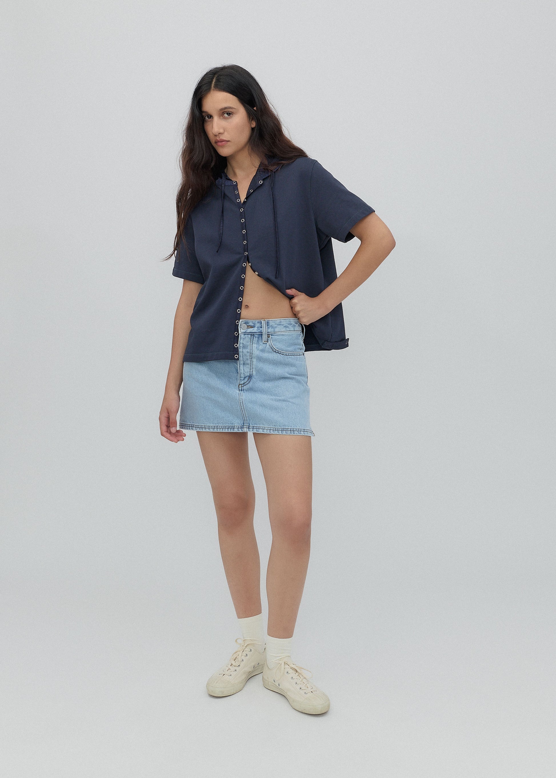 Woman wearing a navy shirt and light blue denim skirt on a white background