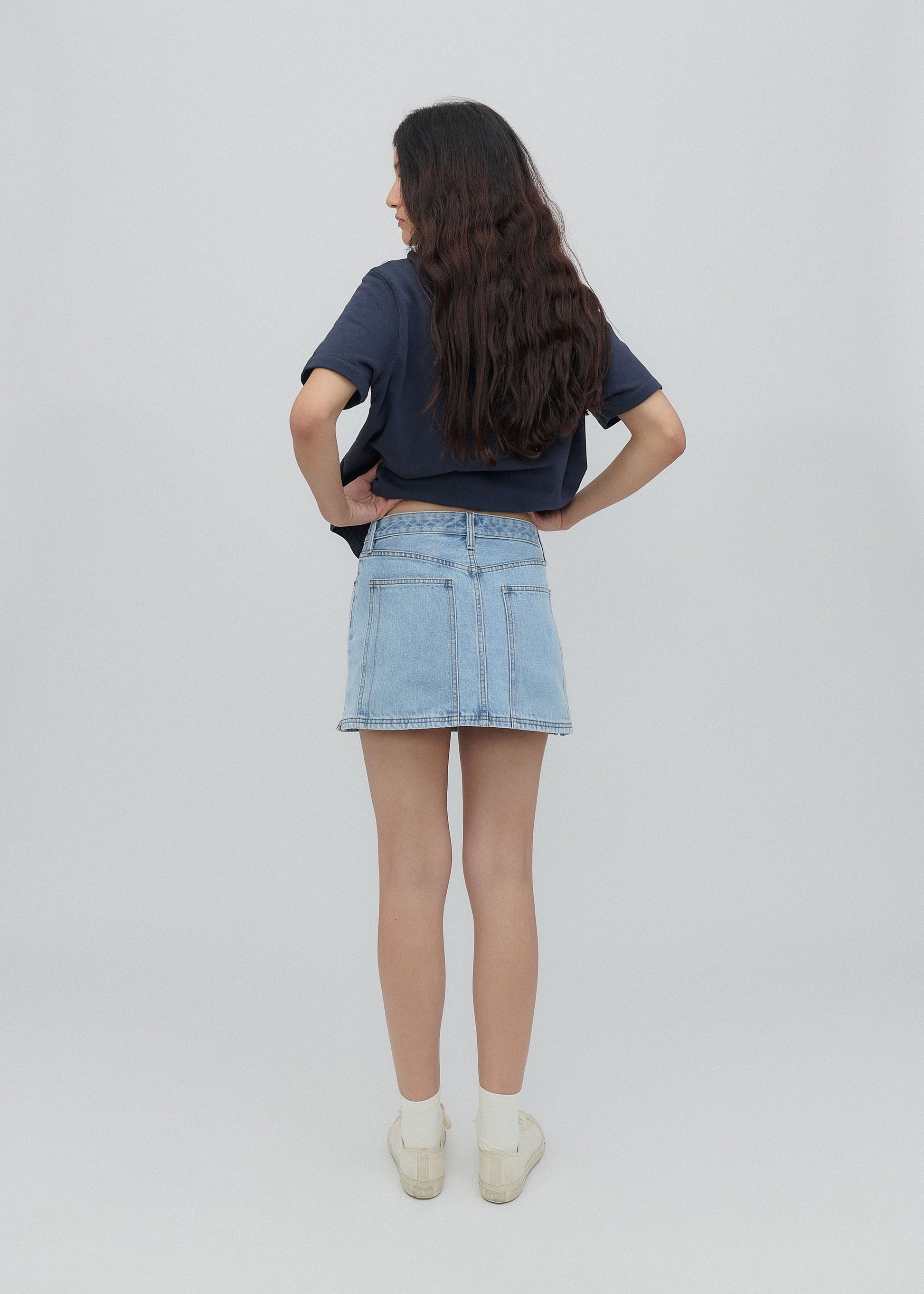 Person wearing a navy blue t-shirt and light blue denim skirt on a plain background