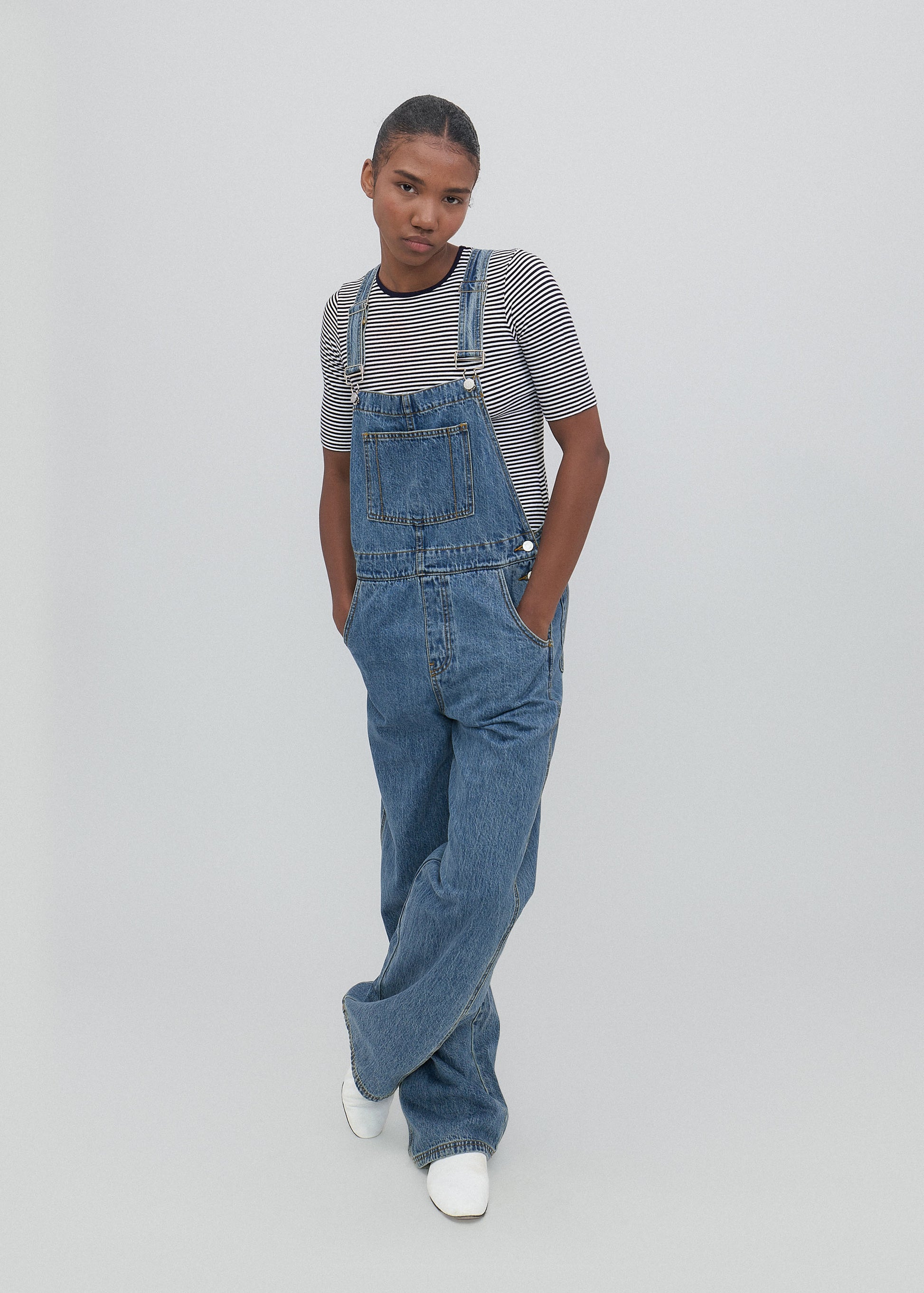 Person wearing blue denim overalls and a striped shirt on a plain background