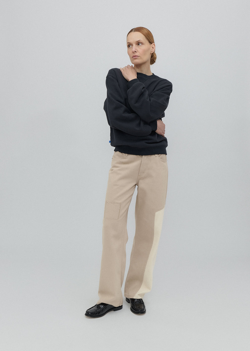 Woman wearing a dark sweater and beige pants on a light gray background