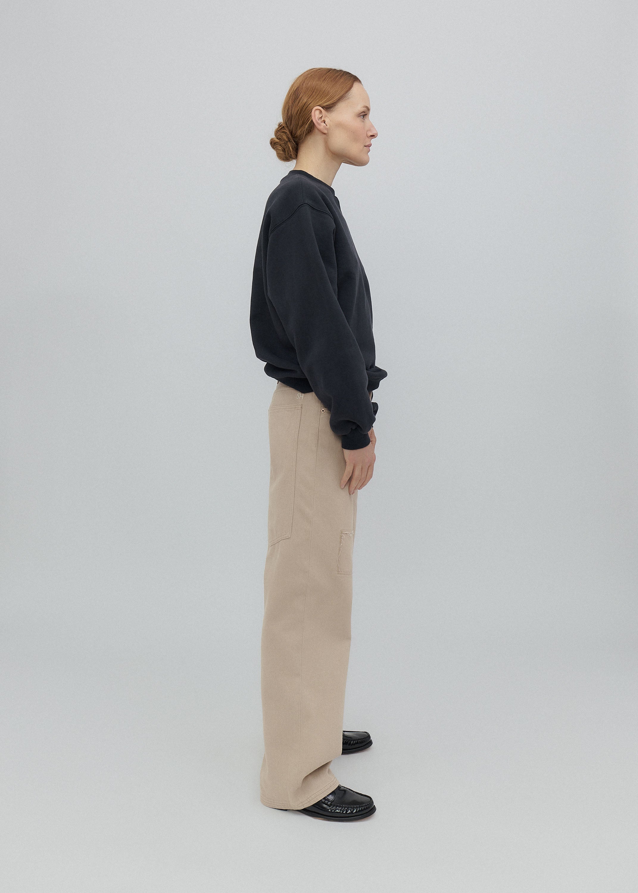 Person wearing a dark sweater and beige pants on a light gray background