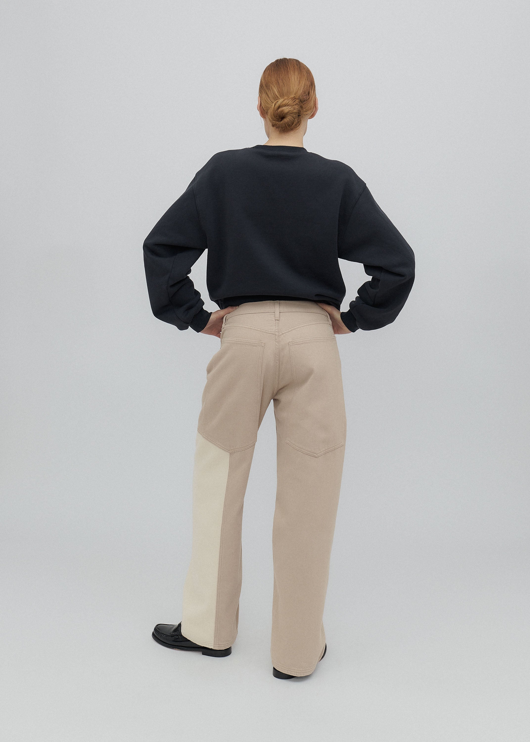 Person wearing a black sweater and beige pants on a white background