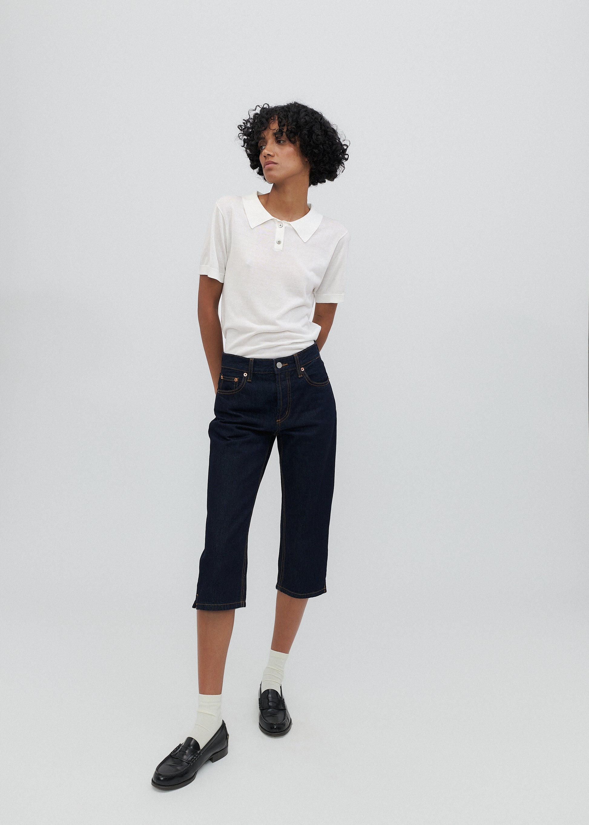 Person wearing a white polo shirt, black pants, and black loafers on a plain background