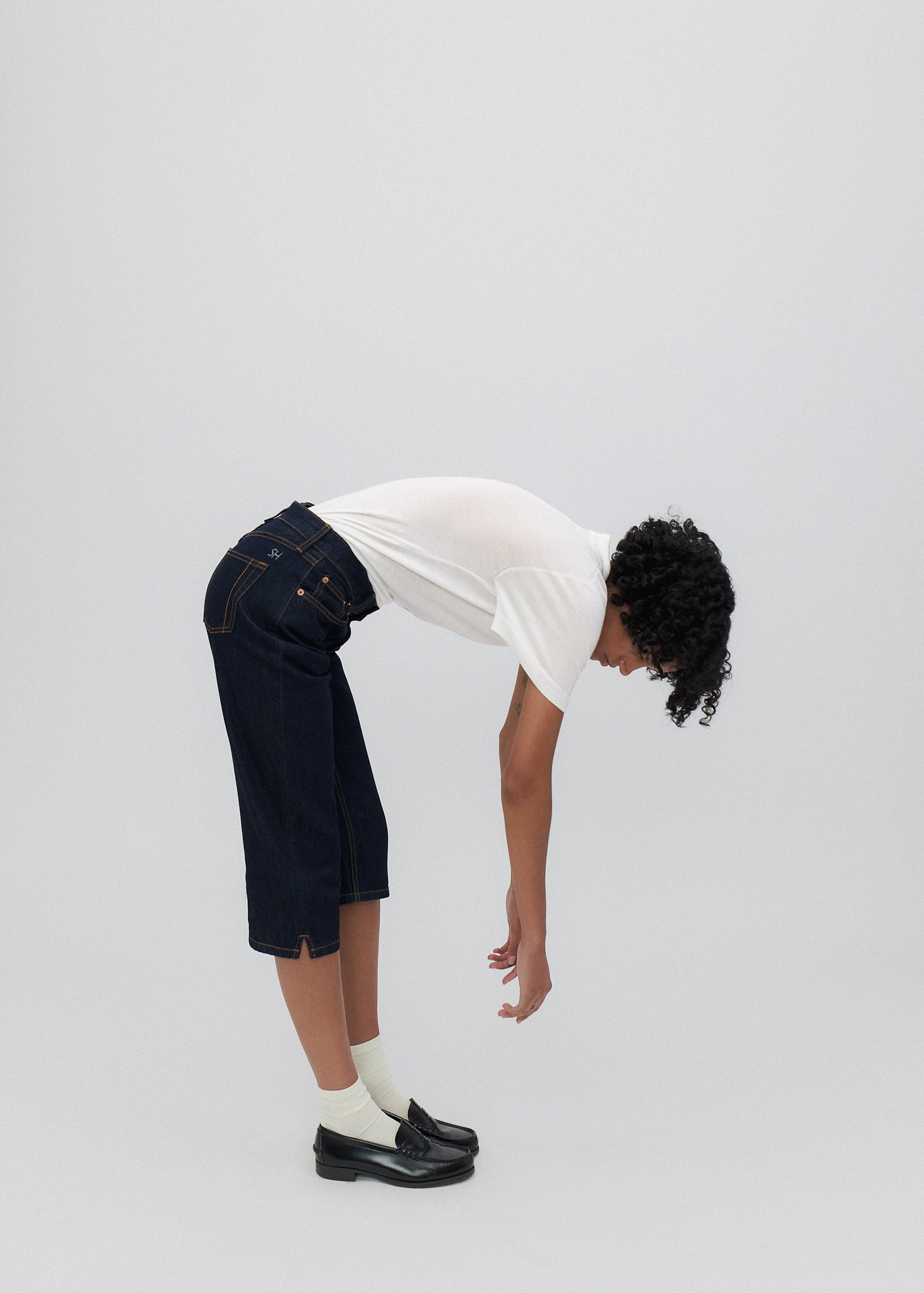 Person wearing a white t-shirt, dark shorts, and black shoes on a plain background