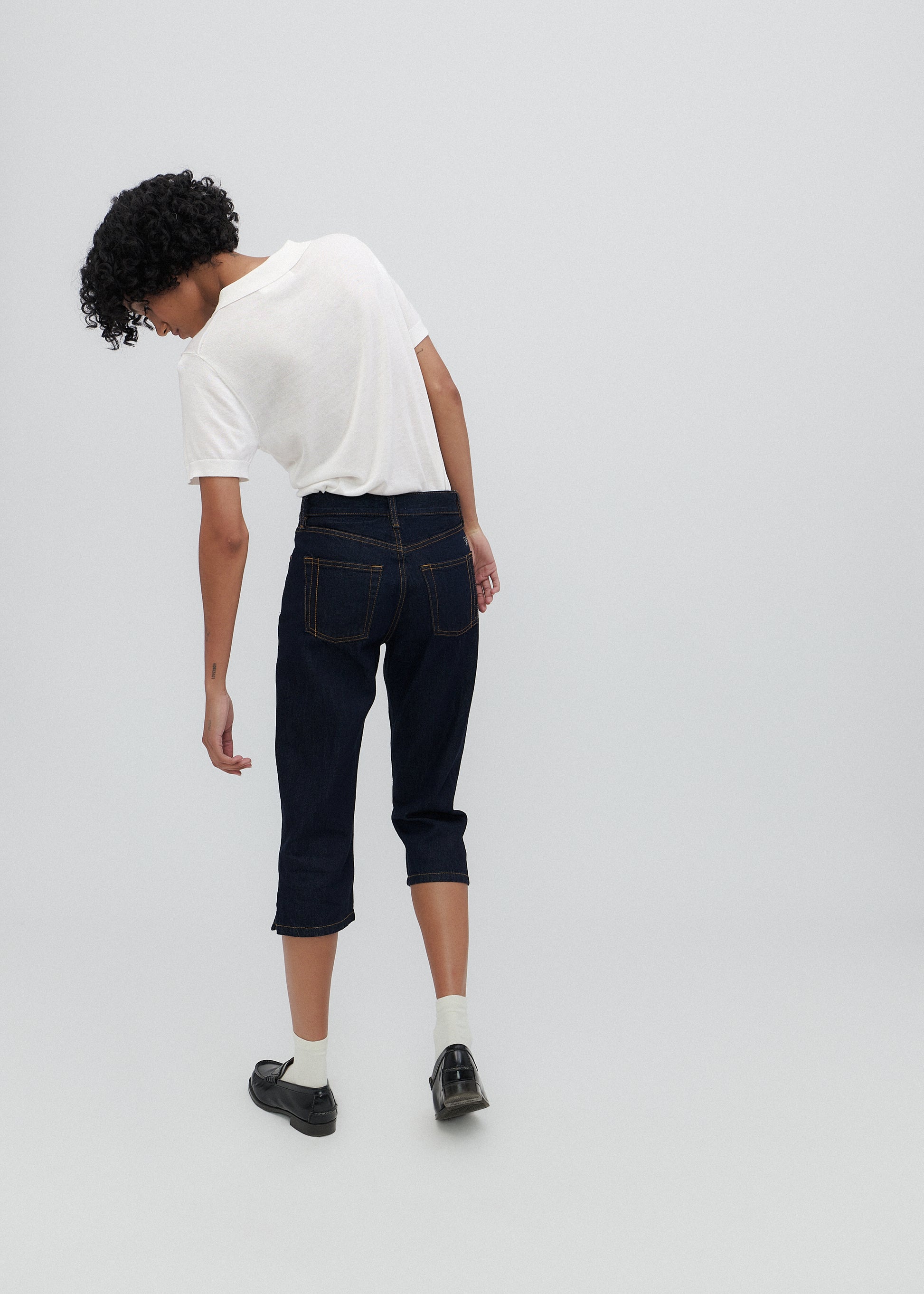 Person wearing a white t-shirt and dark jeans on a plain background