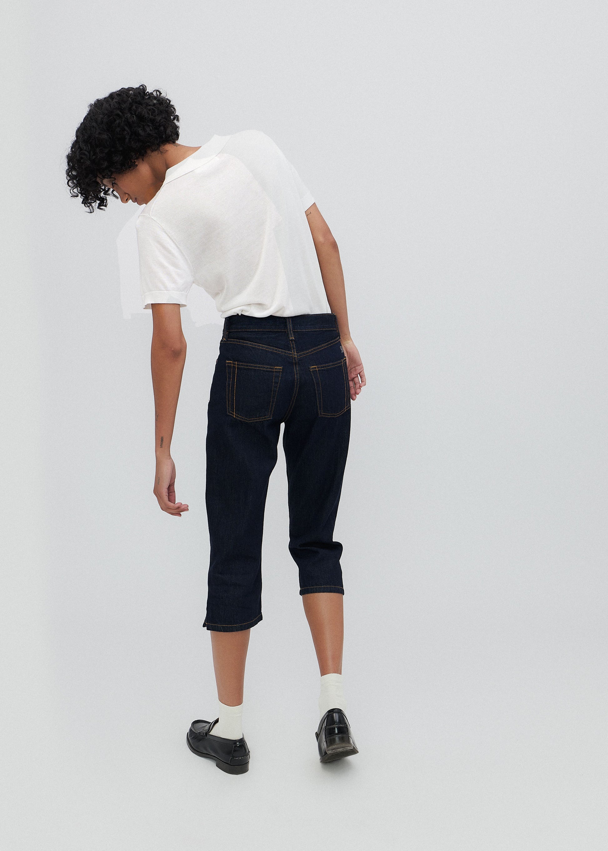 Person wearing a white shirt and dark jeans on a light gray background
