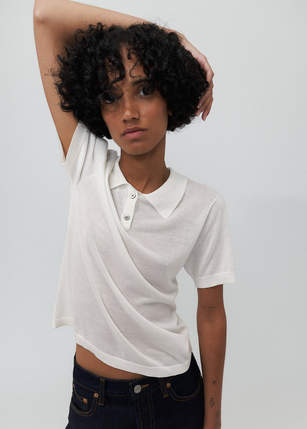 Person wearing a white polo shirt with a draped design on a plain background