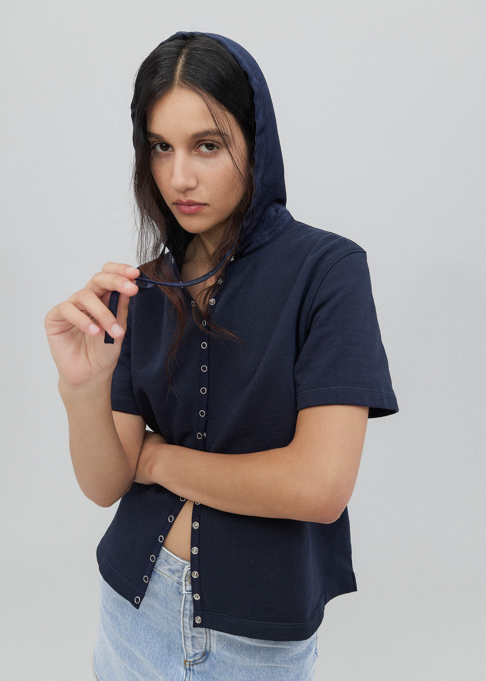 Woman wearing a navy blue hooded shirt with button details on a plain background