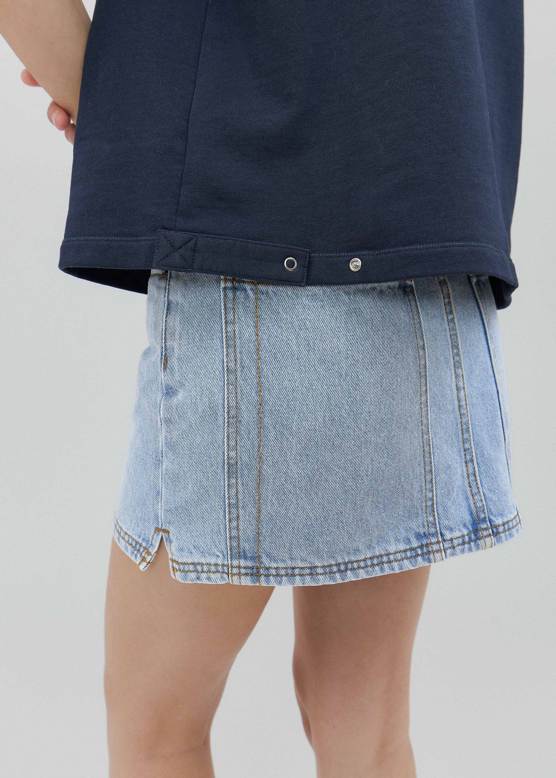 Person wearing a navy shirt and light blue denim skirt on a plain background