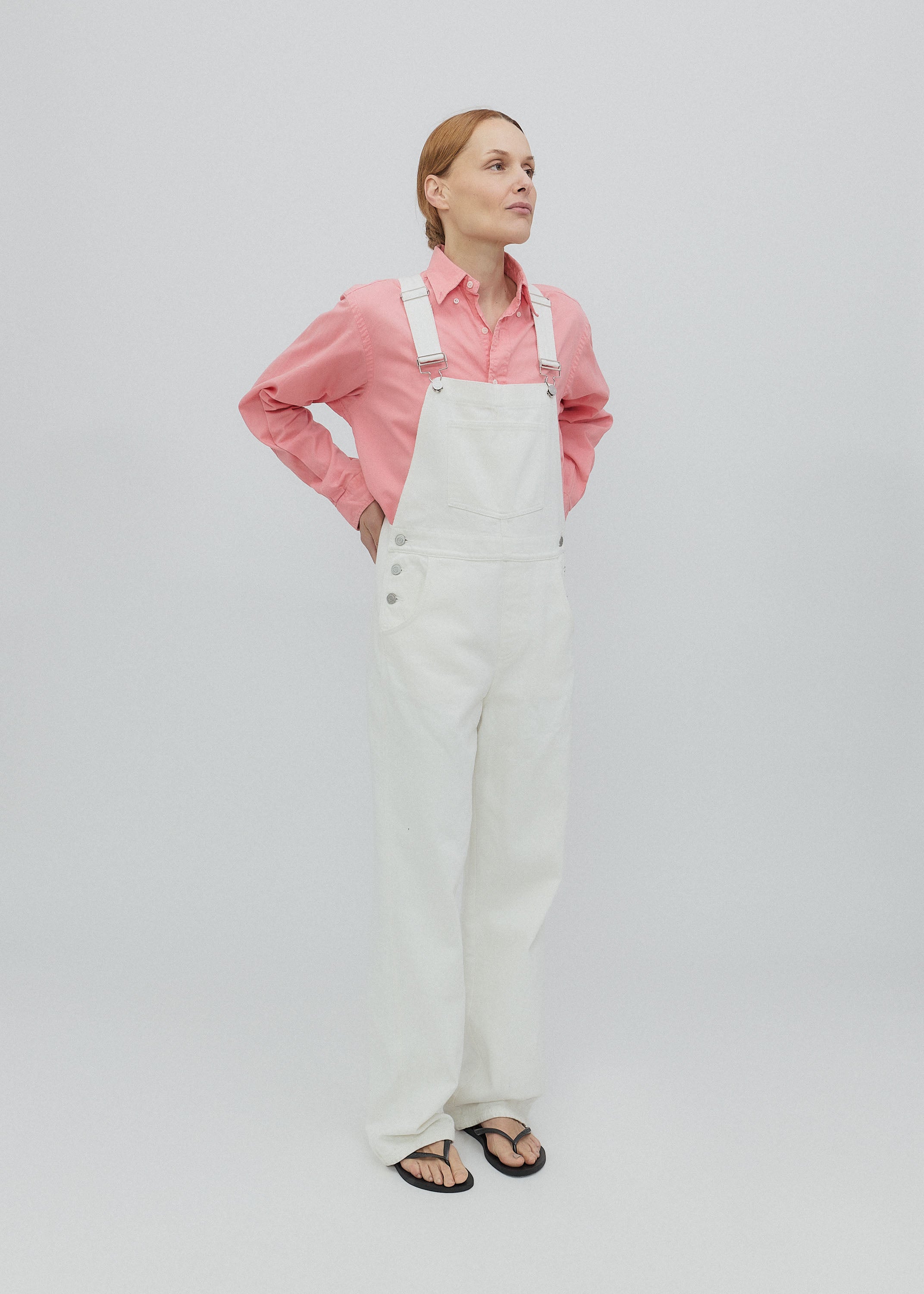 Woman wearing a pink shirt and white overalls on a light gray background