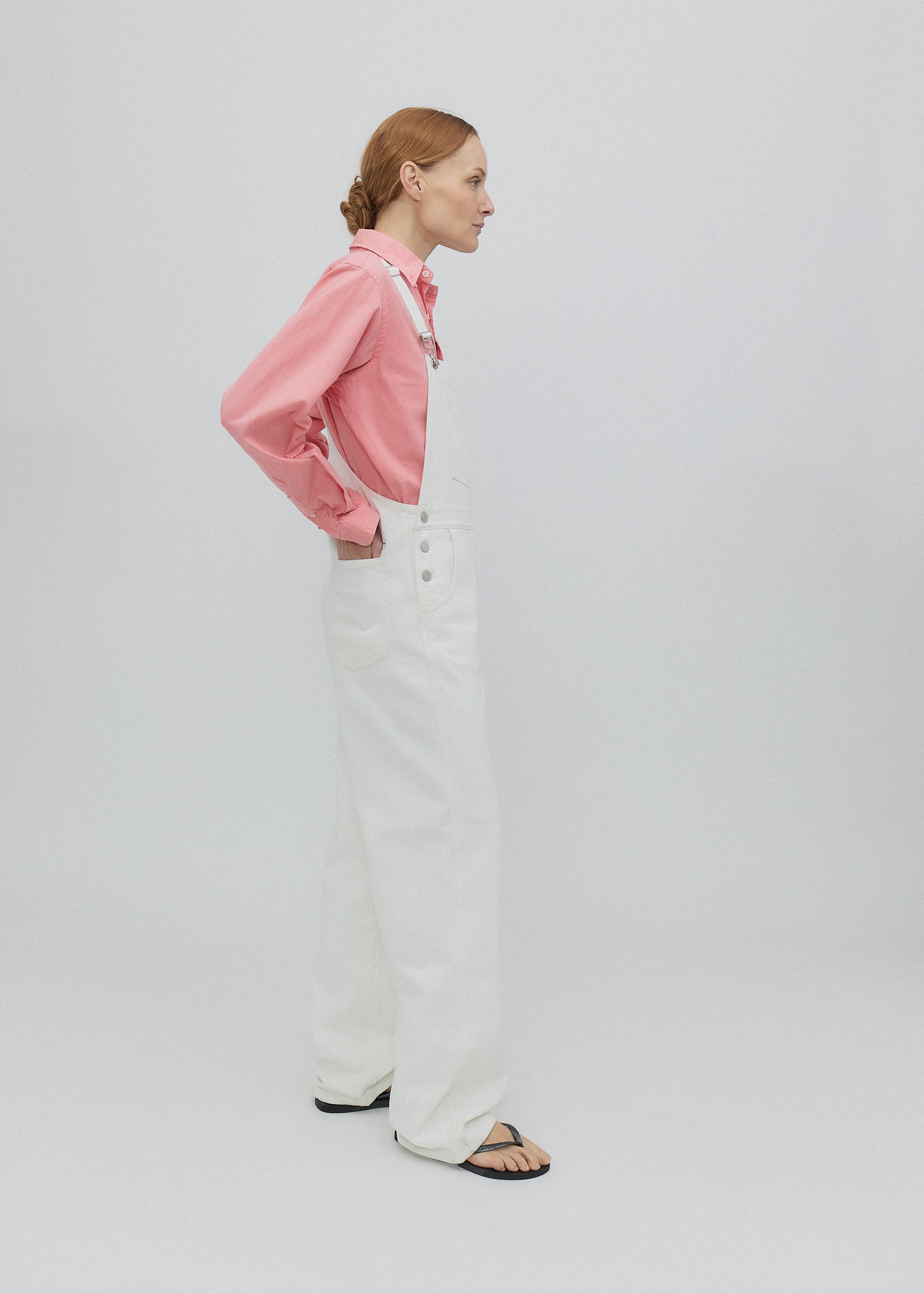 Woman wearing a pink shirt and white overalls on a plain background
