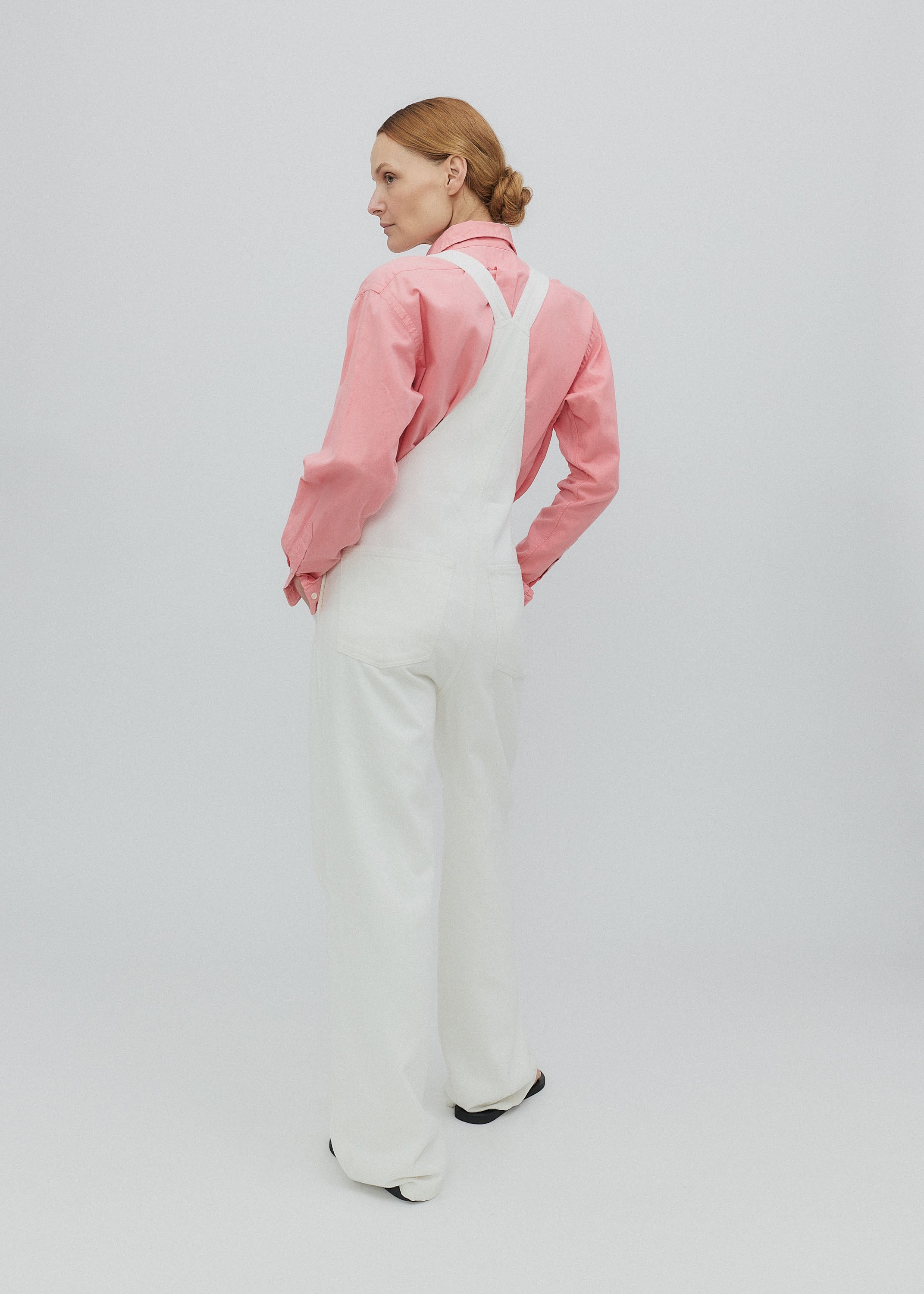 Person wearing a pink jacket and white overalls on a plain background