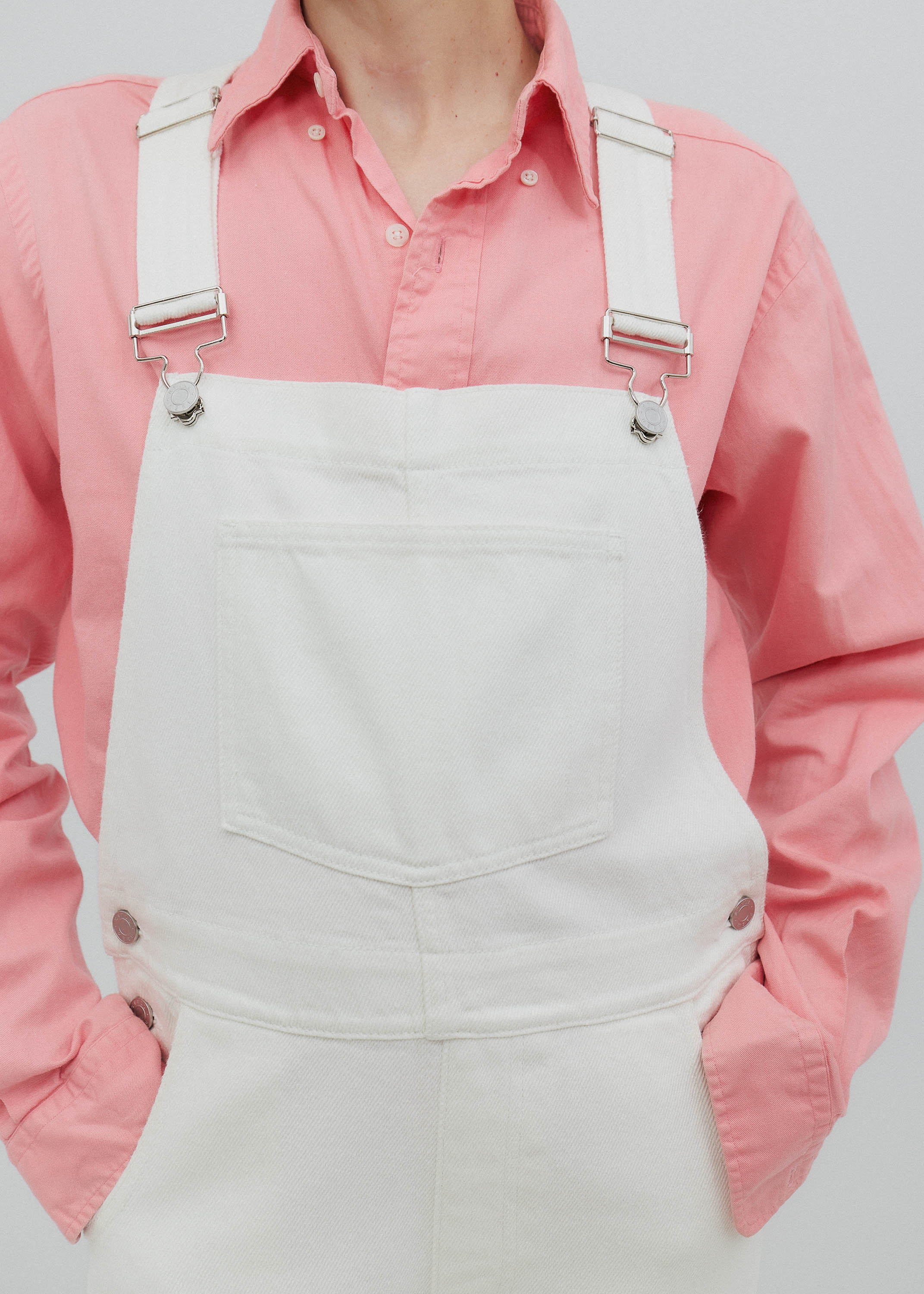 Person wearing a pink shirt and white overalls on a plain background
