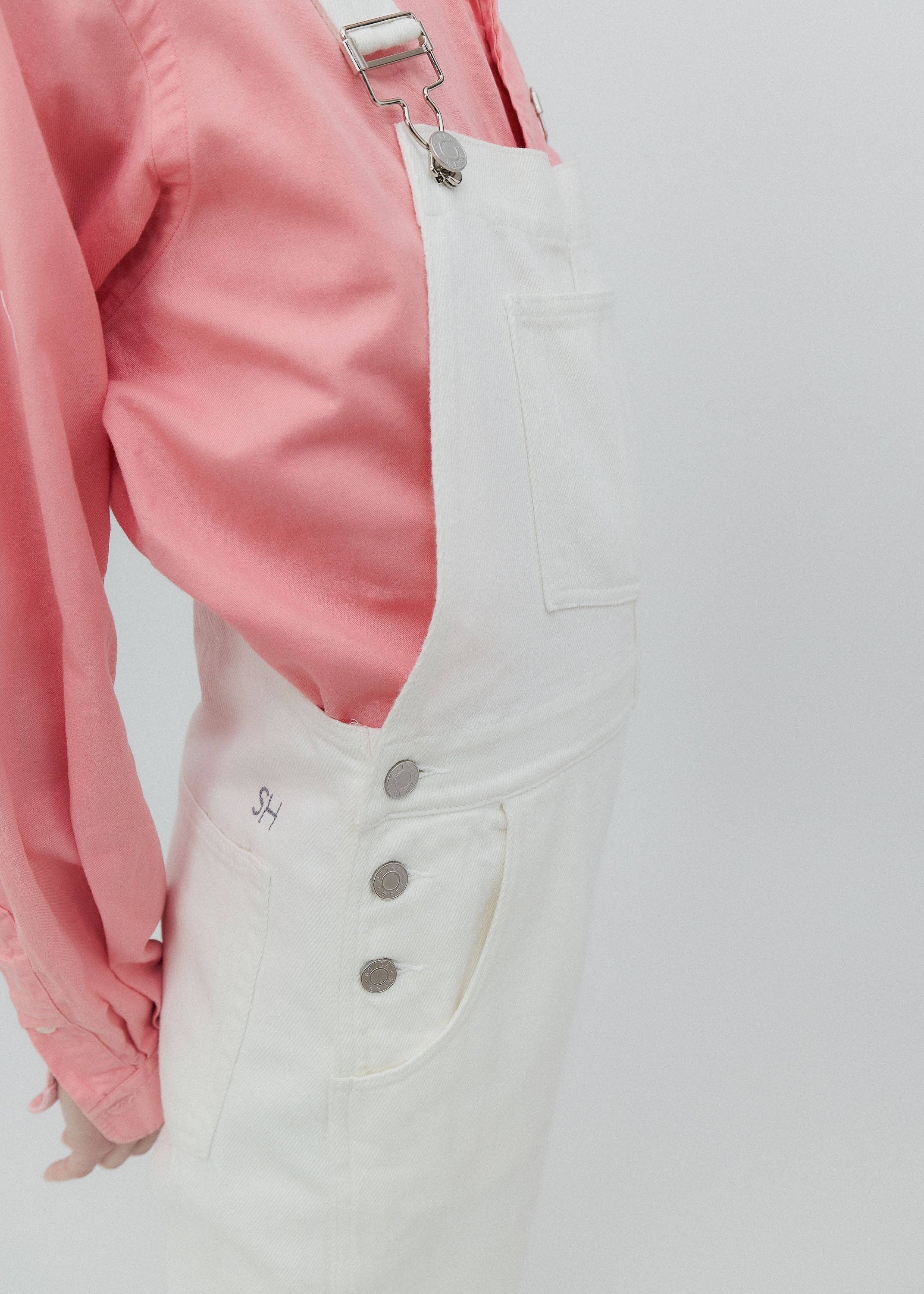 White denim overalls with a pink jacket on a light gray background