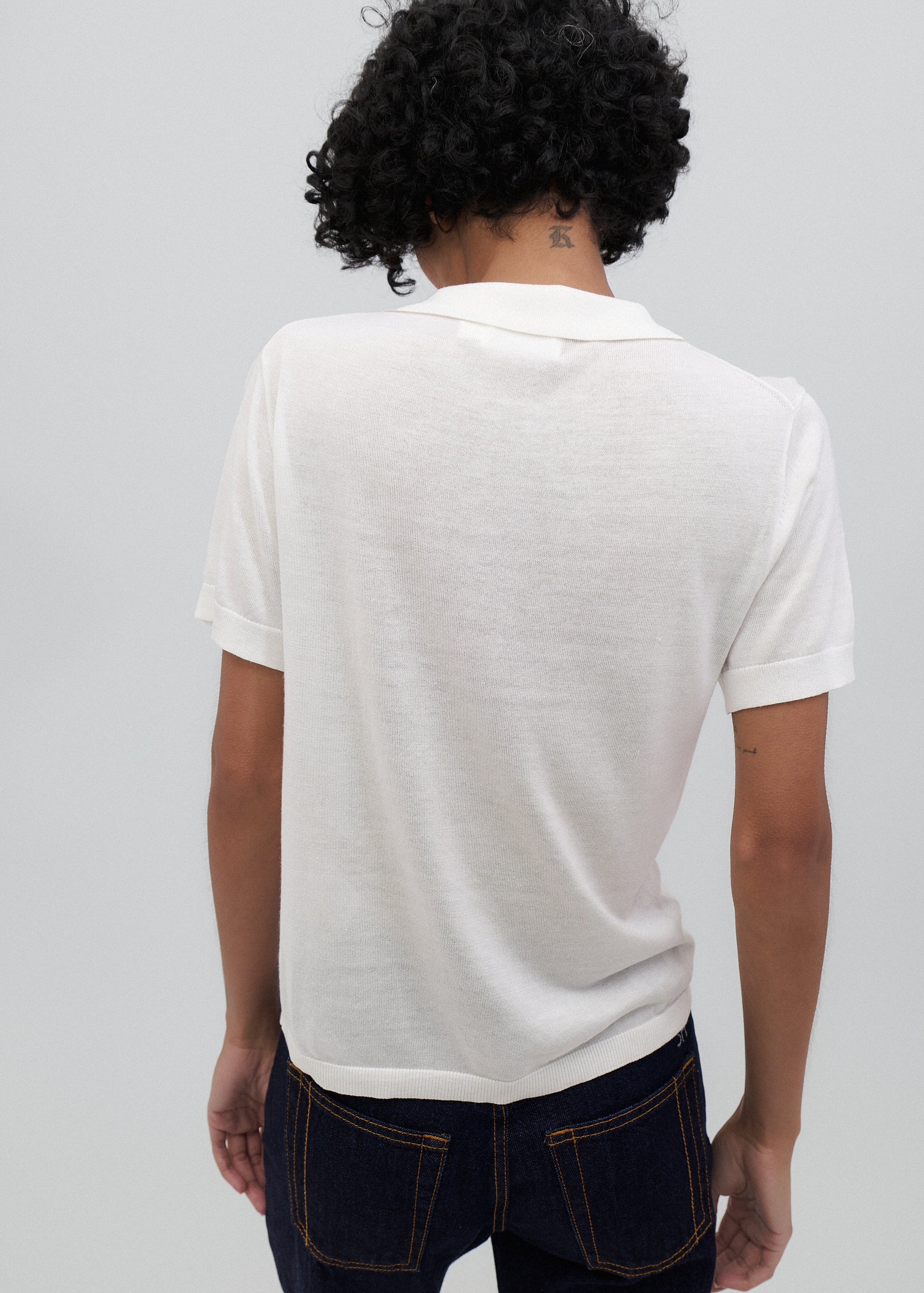 Person wearing a white polo shirt and dark jeans on a plain background