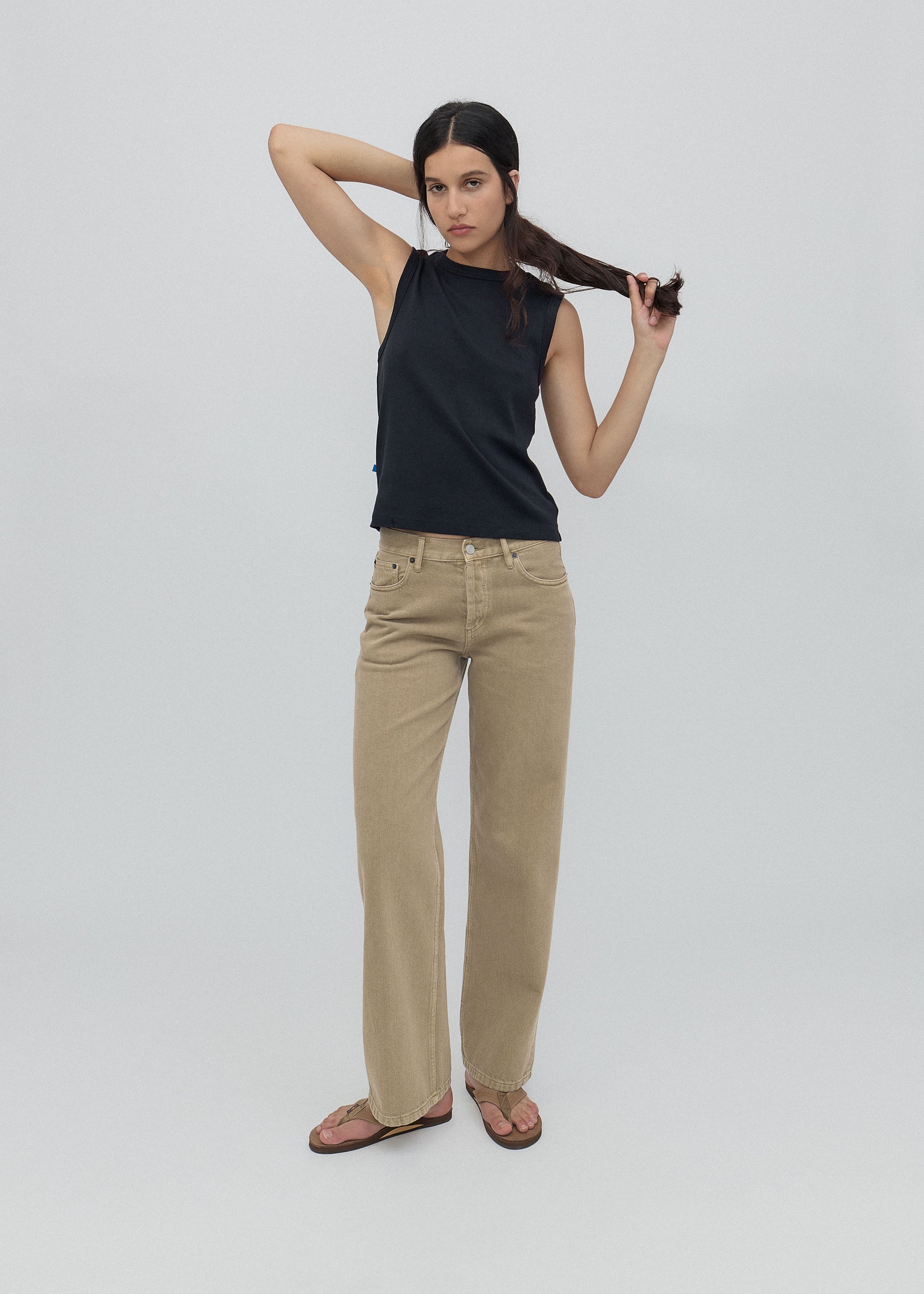 Woman wearing a black sleeveless top and beige pants against a white background