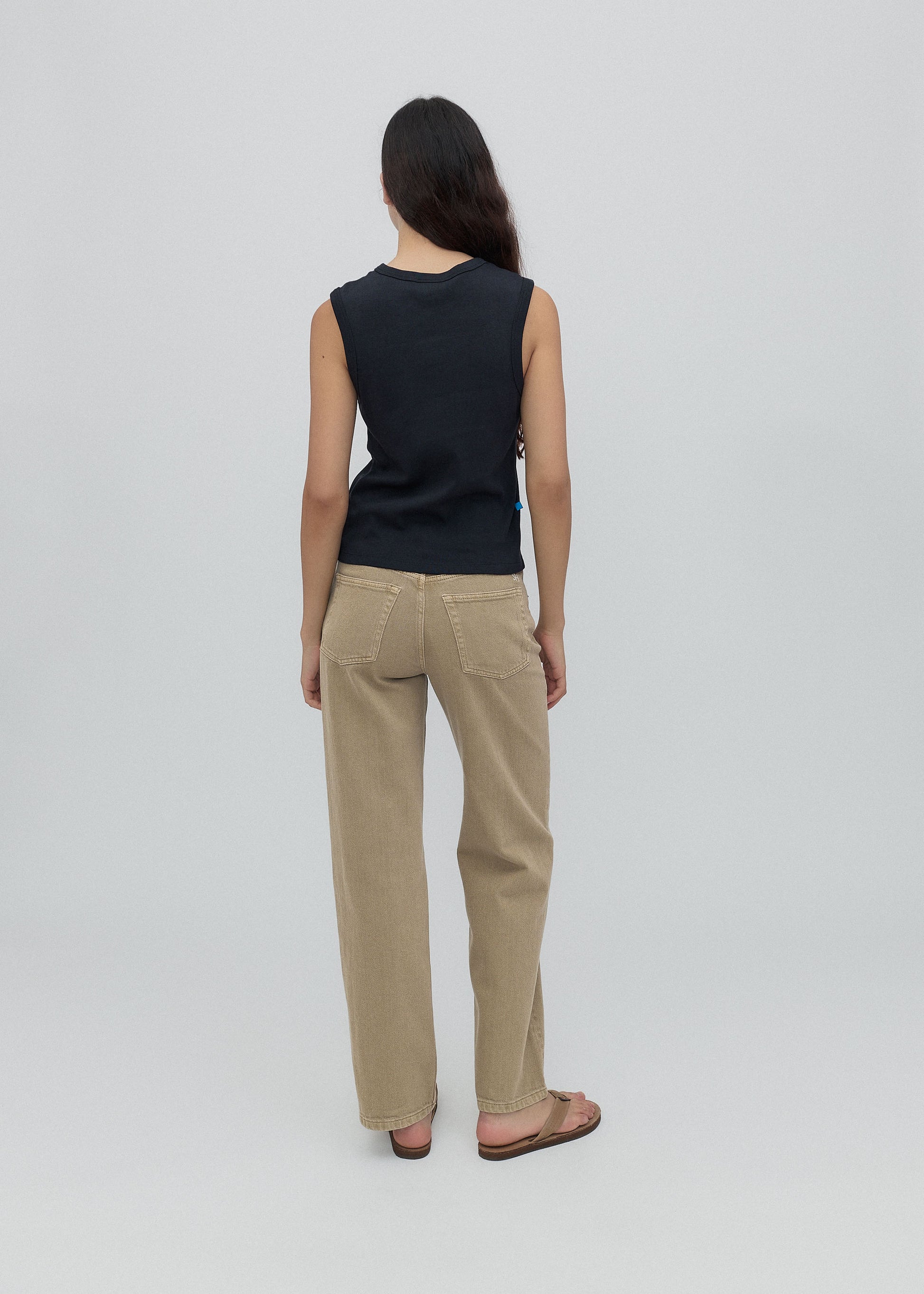 Person wearing a black sleeveless top and beige pants on a light gray background
