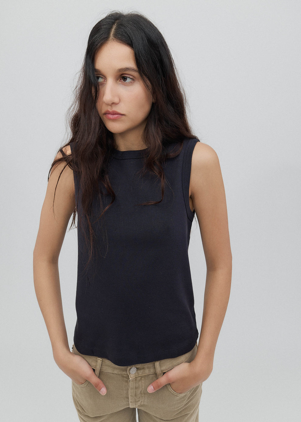 Woman wearing a black sleeveless top and beige pants against a plain background