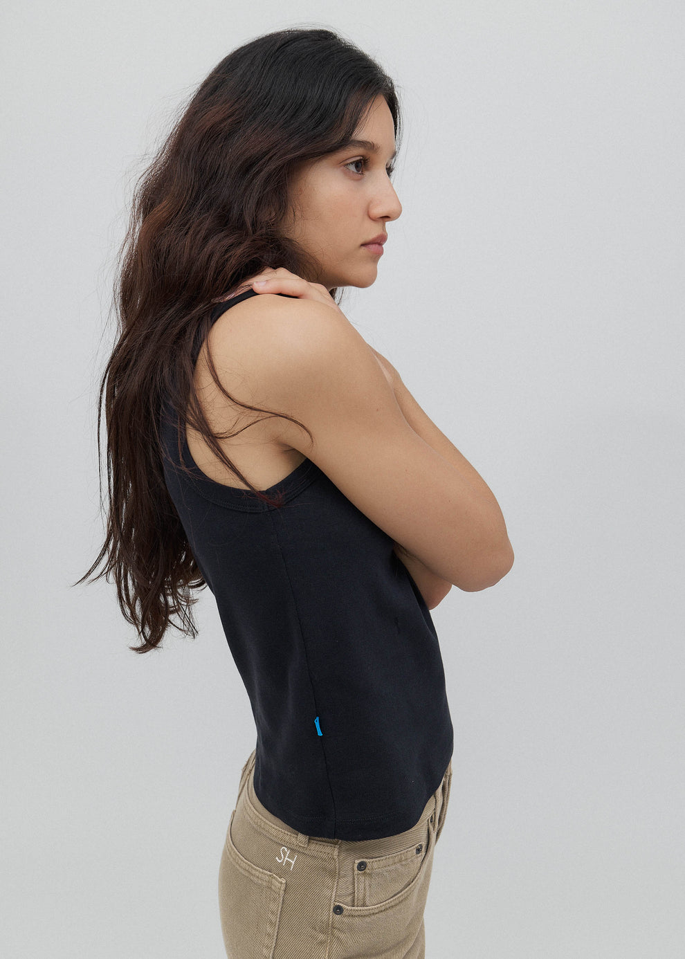 Woman wearing a black tank top and beige pants against a plain background