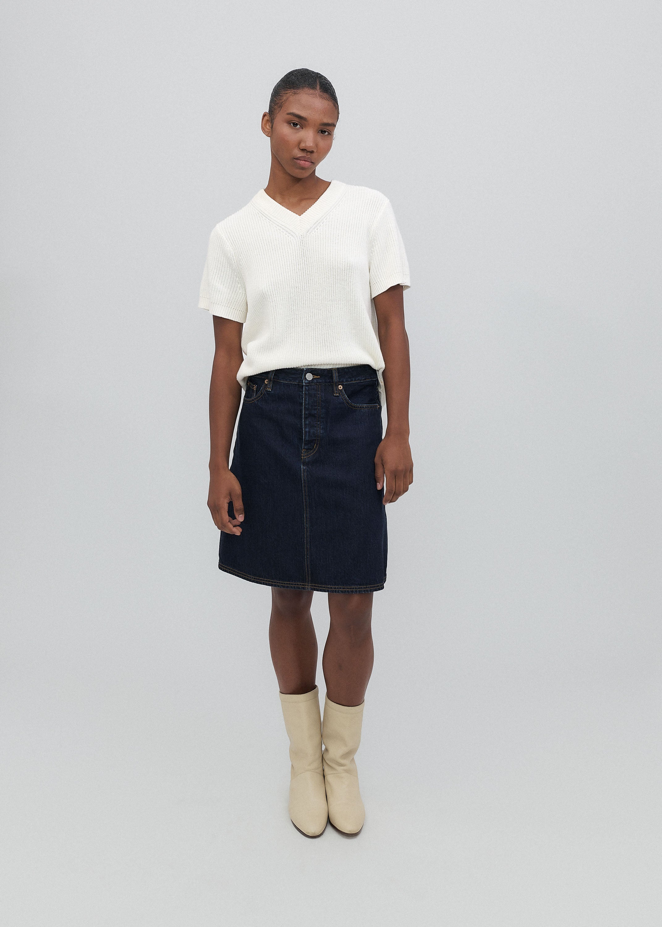 Woman wearing a white top and black skirt with beige boots on a plain background