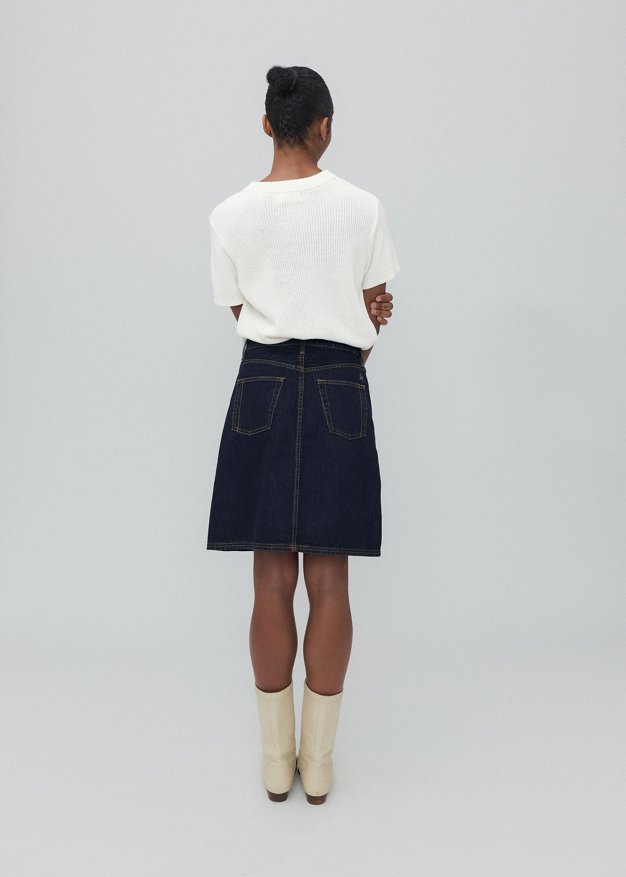 Person wearing a white top and dark denim skirt on a plain background
