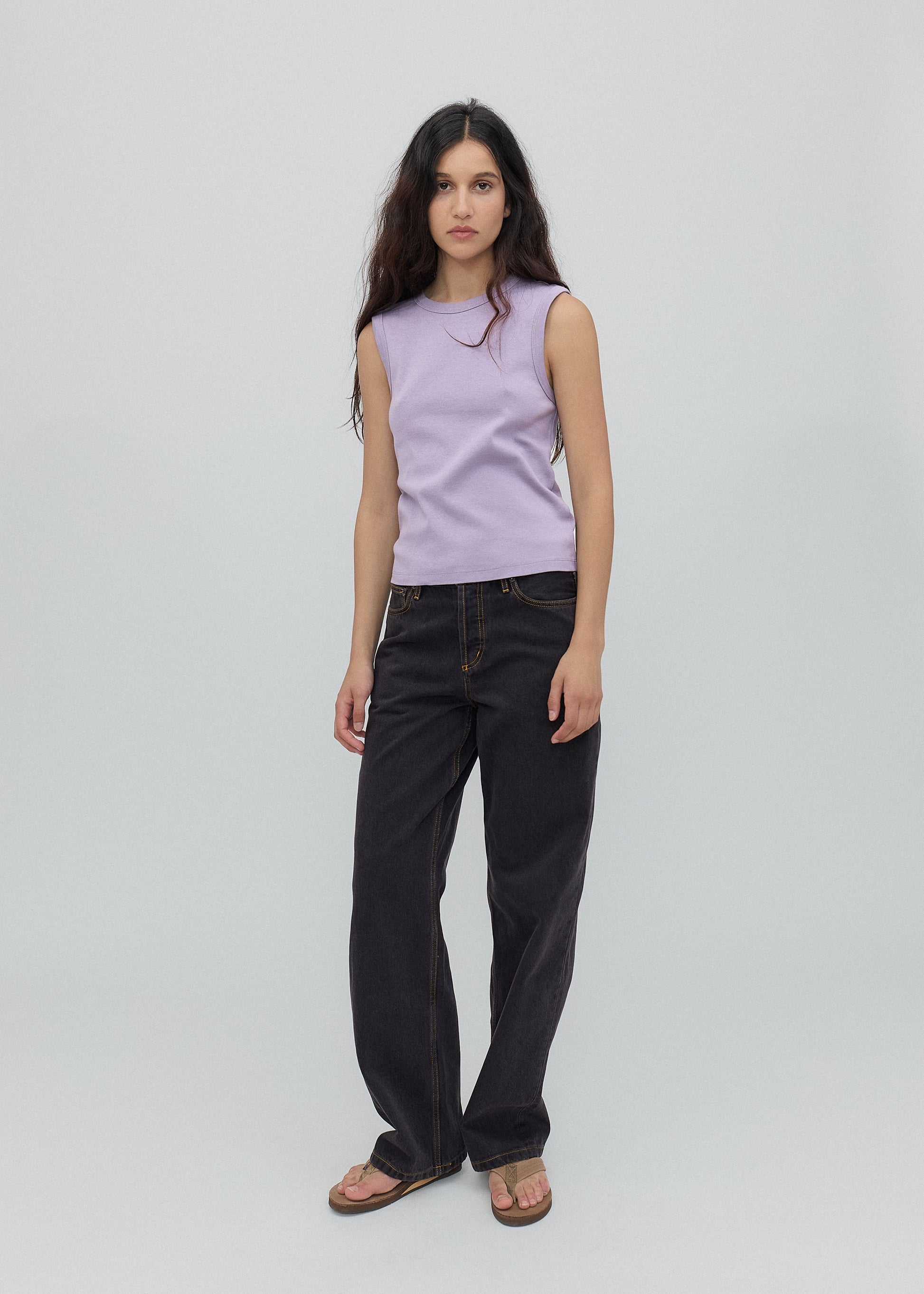 Woman wearing a light purple sleeveless top and black pants on a gray background