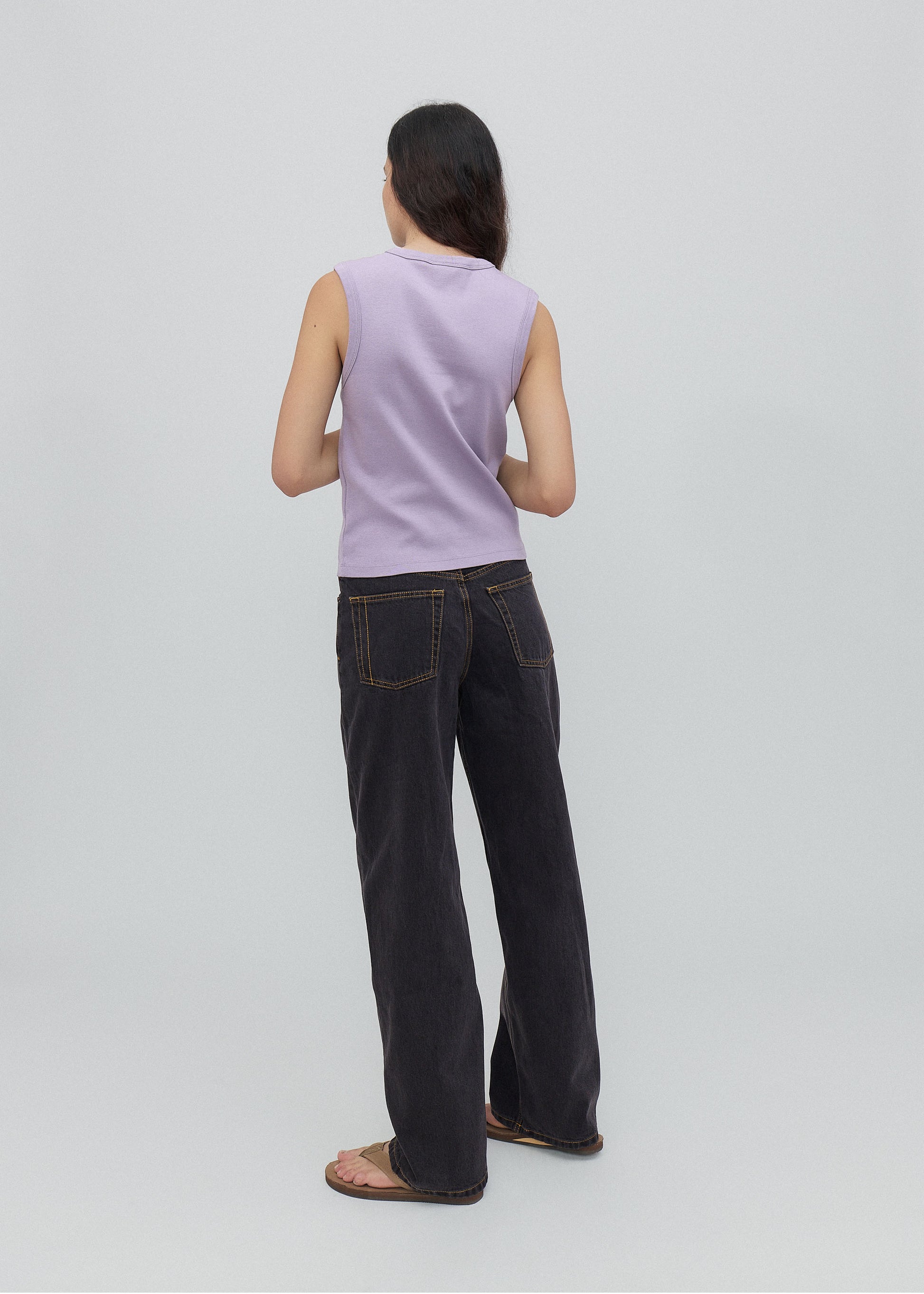Person wearing a light purple sleeveless top and dark jeans on a light gray background