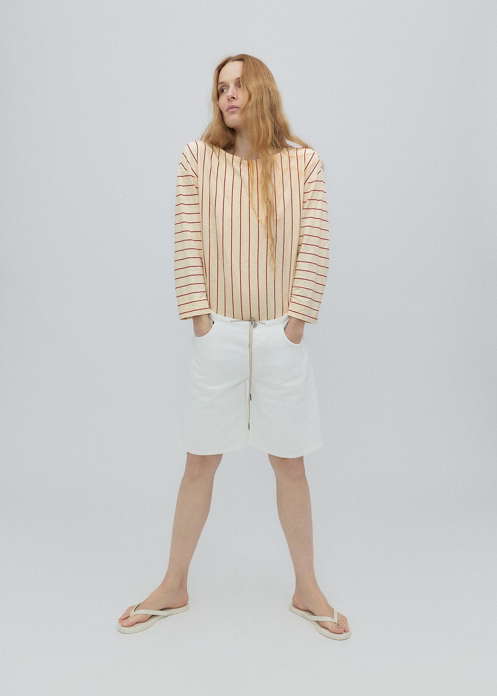 Woman wearing a striped shirt and white pants on a plain background