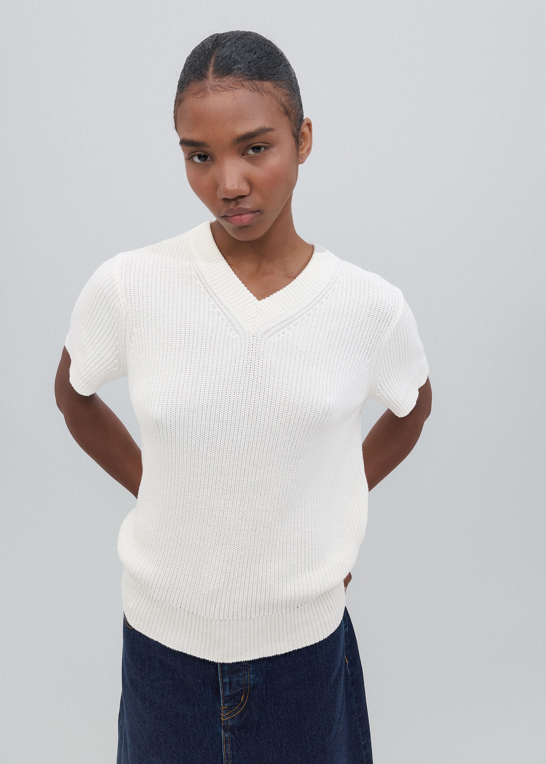 Person wearing a white ribbed sweater and dark pants on a plain background