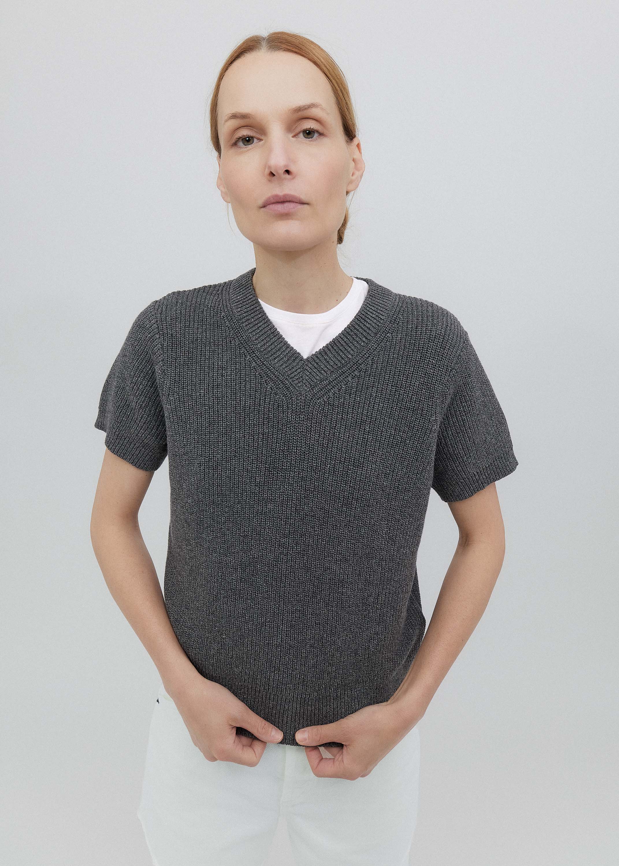 Person wearing a gray knitted sweater over a white shirt on a light gray background