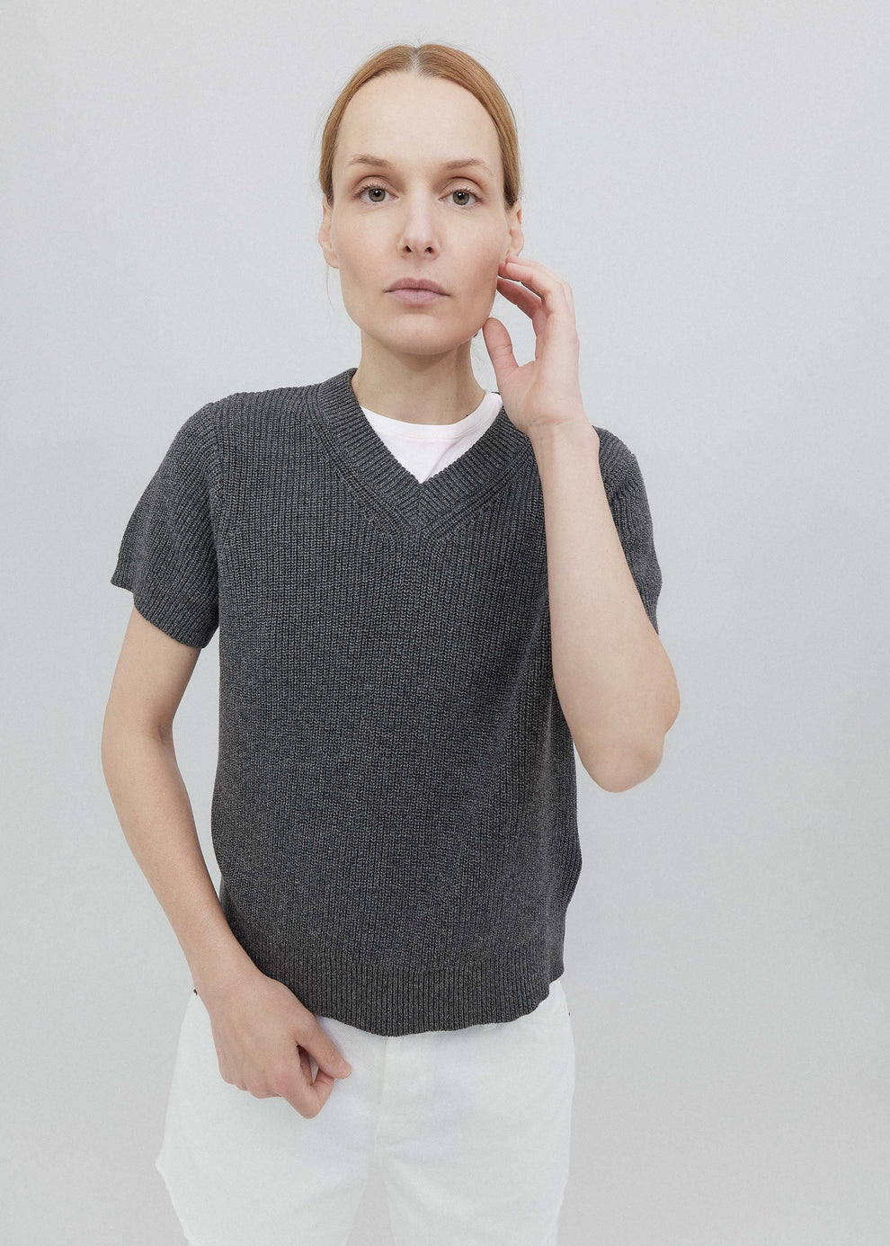 Woman wearing a gray short-sleeve sweater over a white shirt on a light gray background