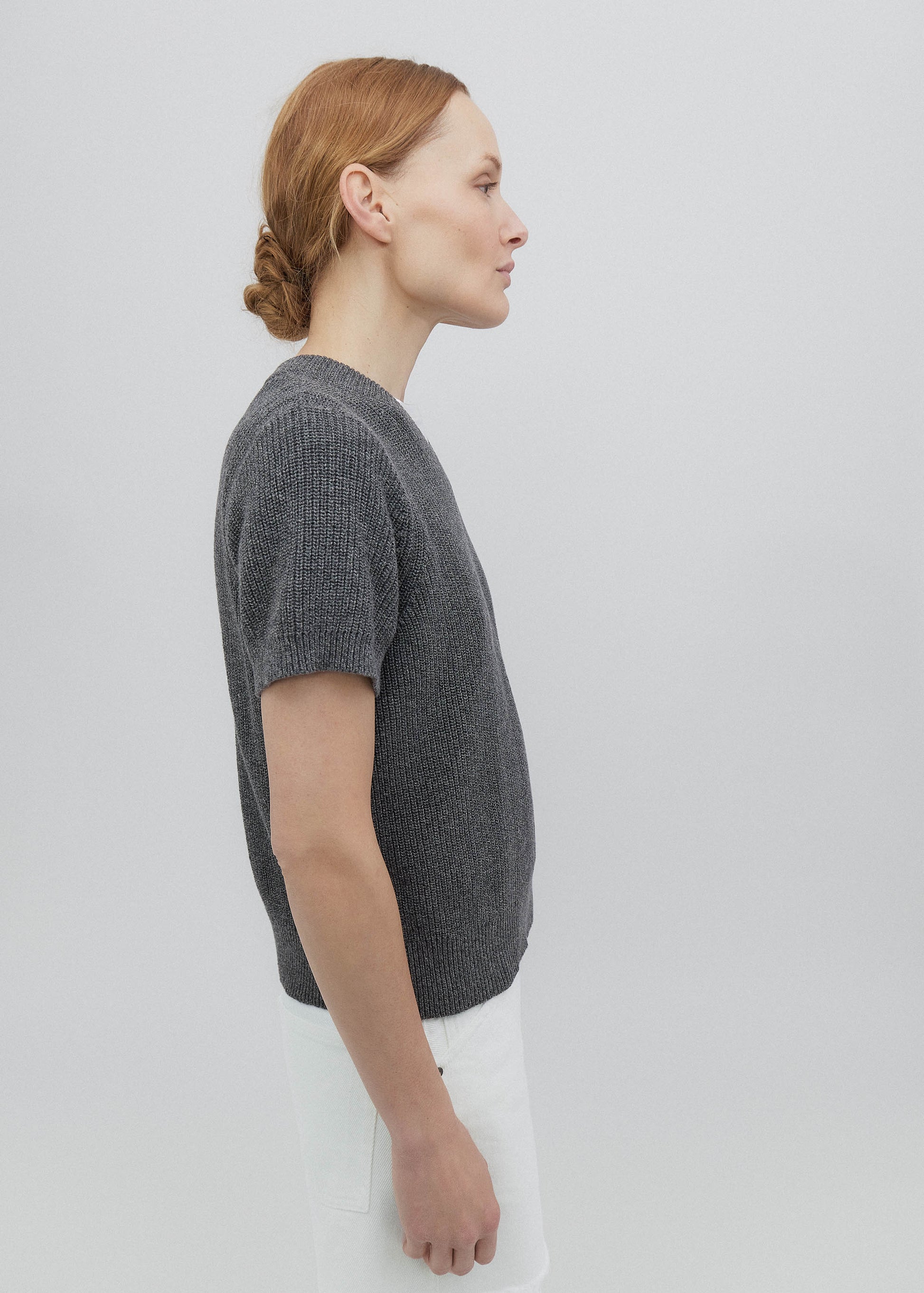 Person wearing a gray knitted sweater against a plain background