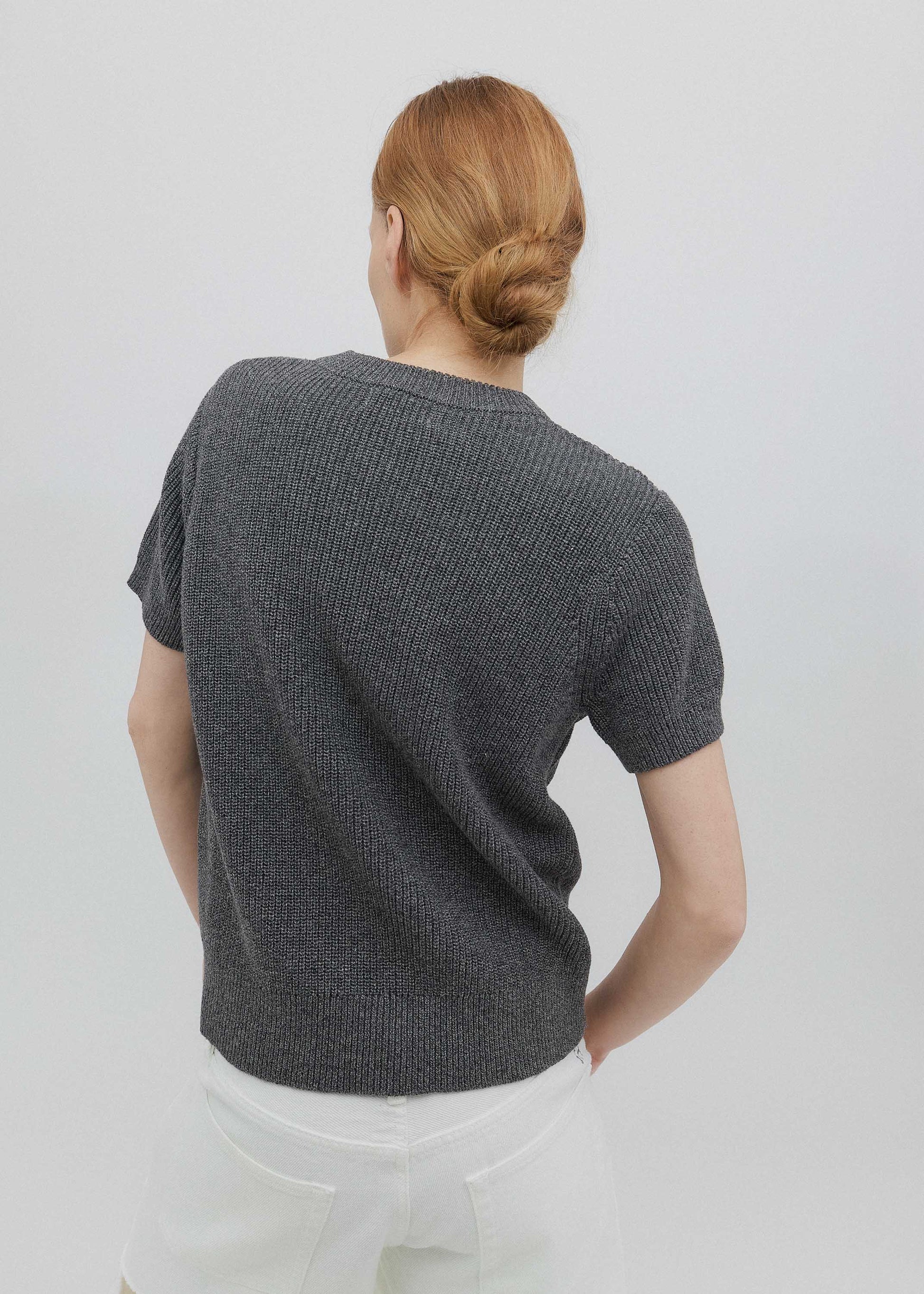 Person wearing a dark gray knitted sweater against a plain background
