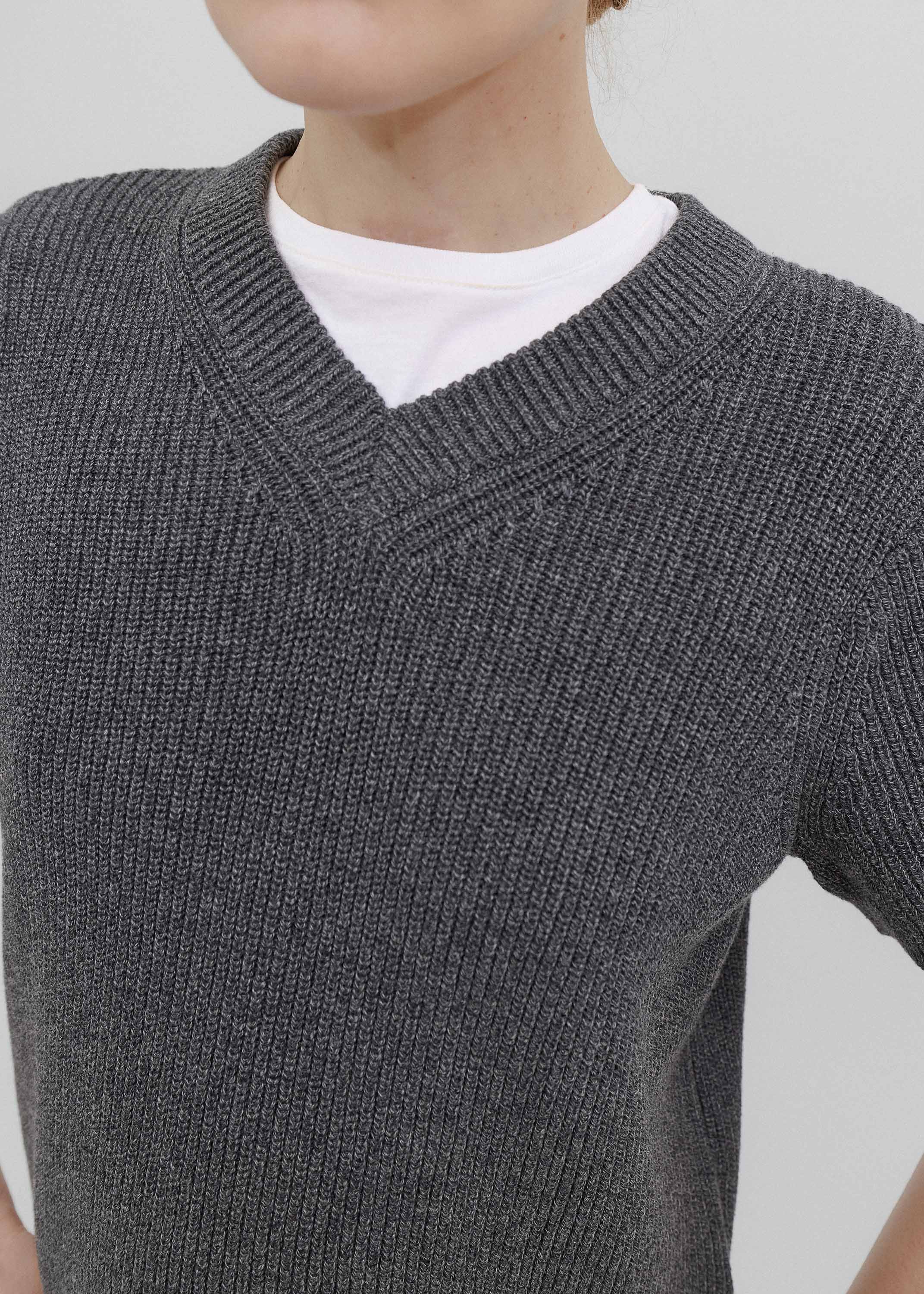 Person wearing a gray knitted sweater over a white shirt on a plain background