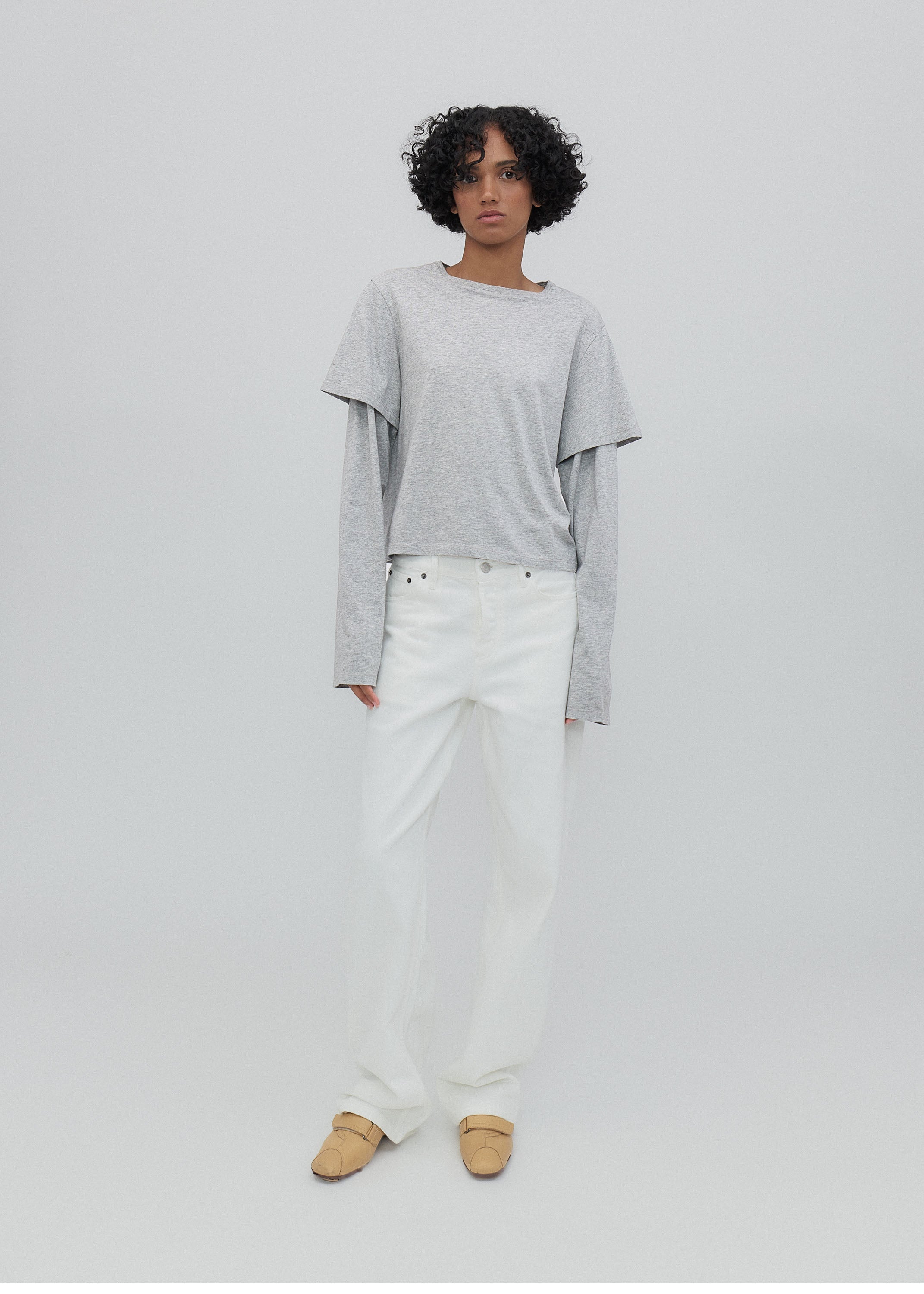 Person wearing a gray long-sleeve top and white pants on a plain background