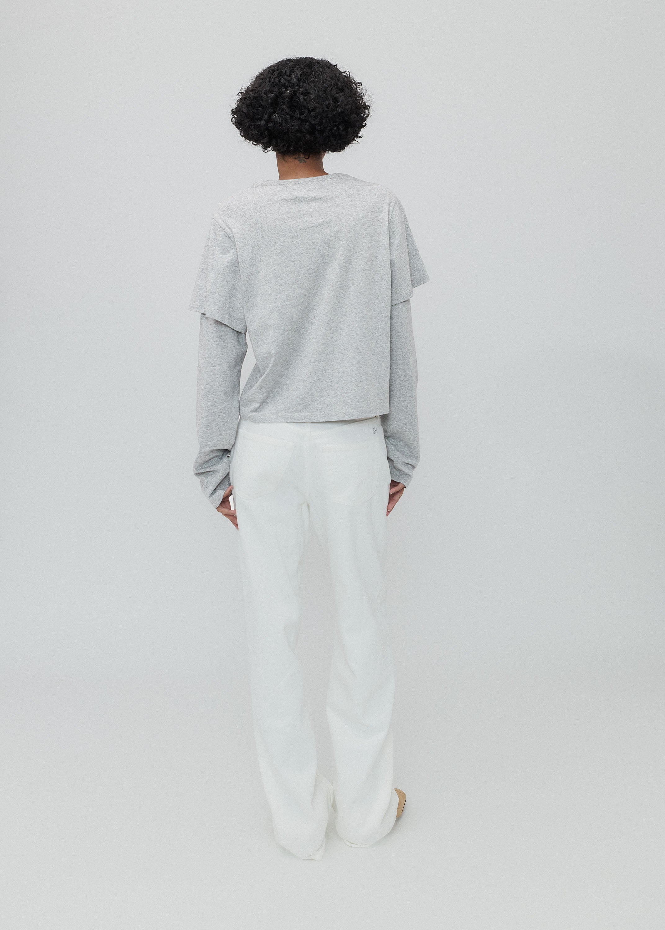 Person wearing a light gray oversized shirt and white pants on a plain background