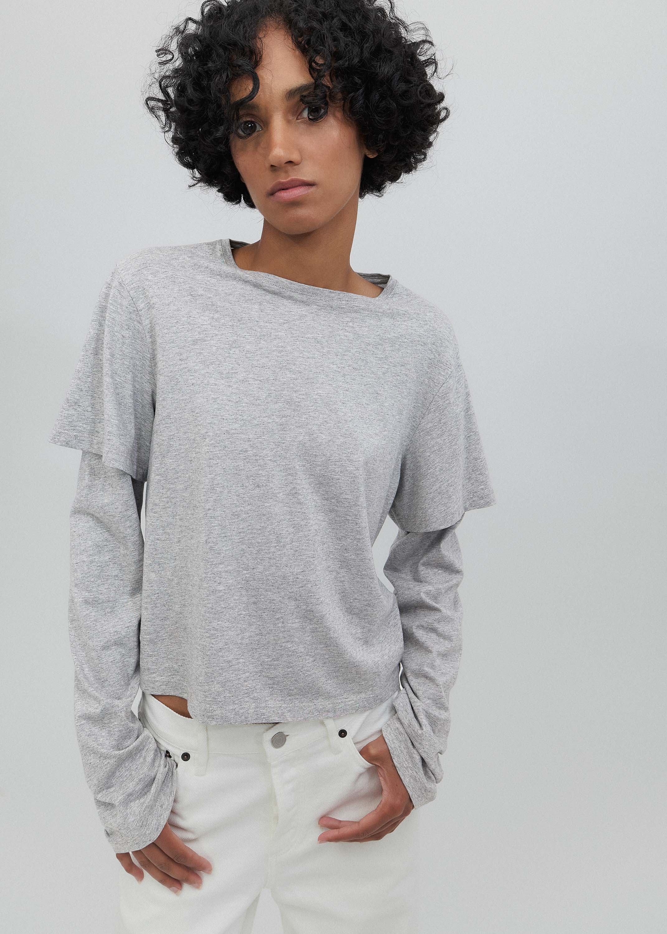Person wearing a gray long-sleeve shirt and white pants on a plain background