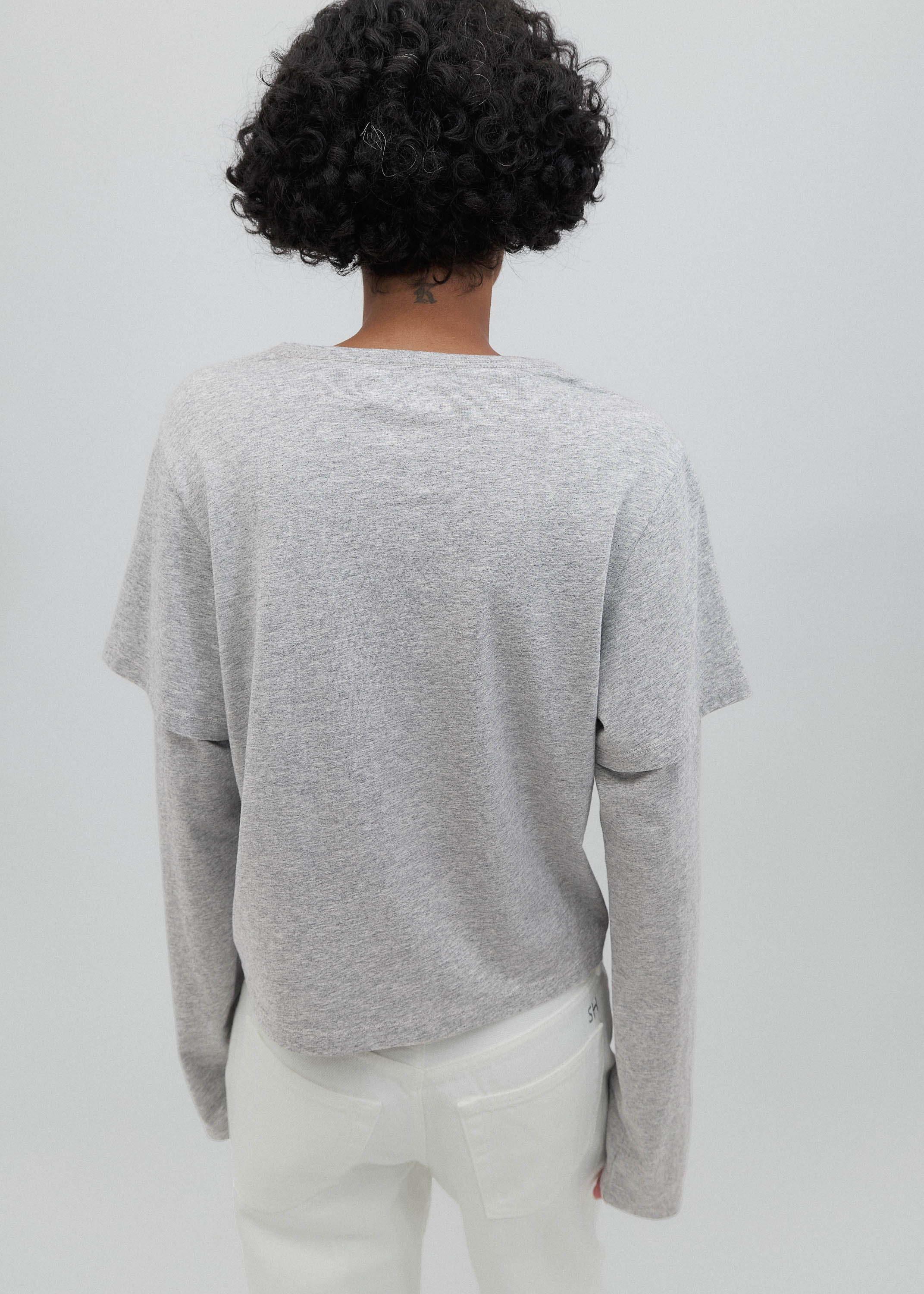 Person wearing a gray sweater and white pants against a plain background