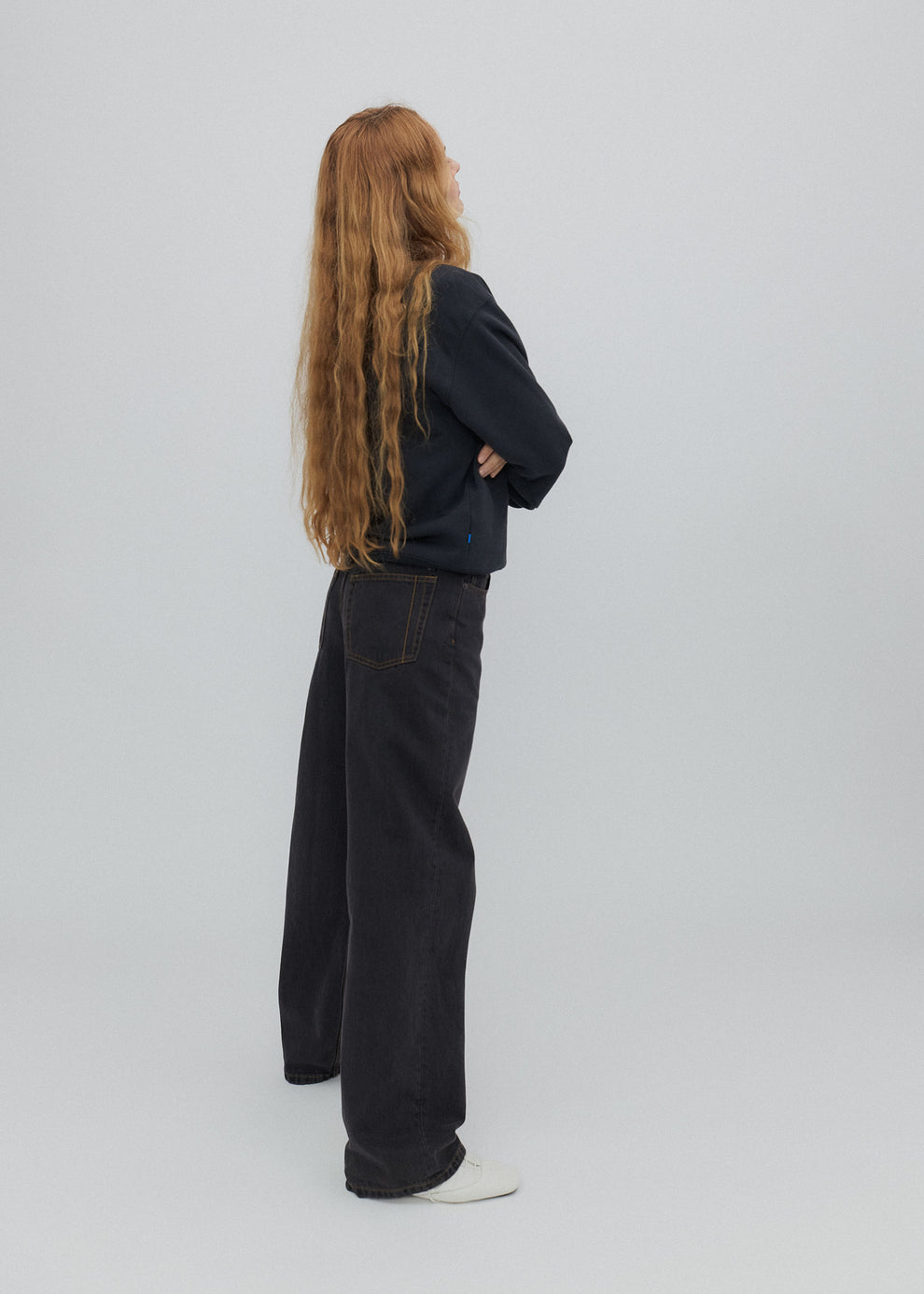 Person wearing a black jacket and dark jeans standing against a plain background