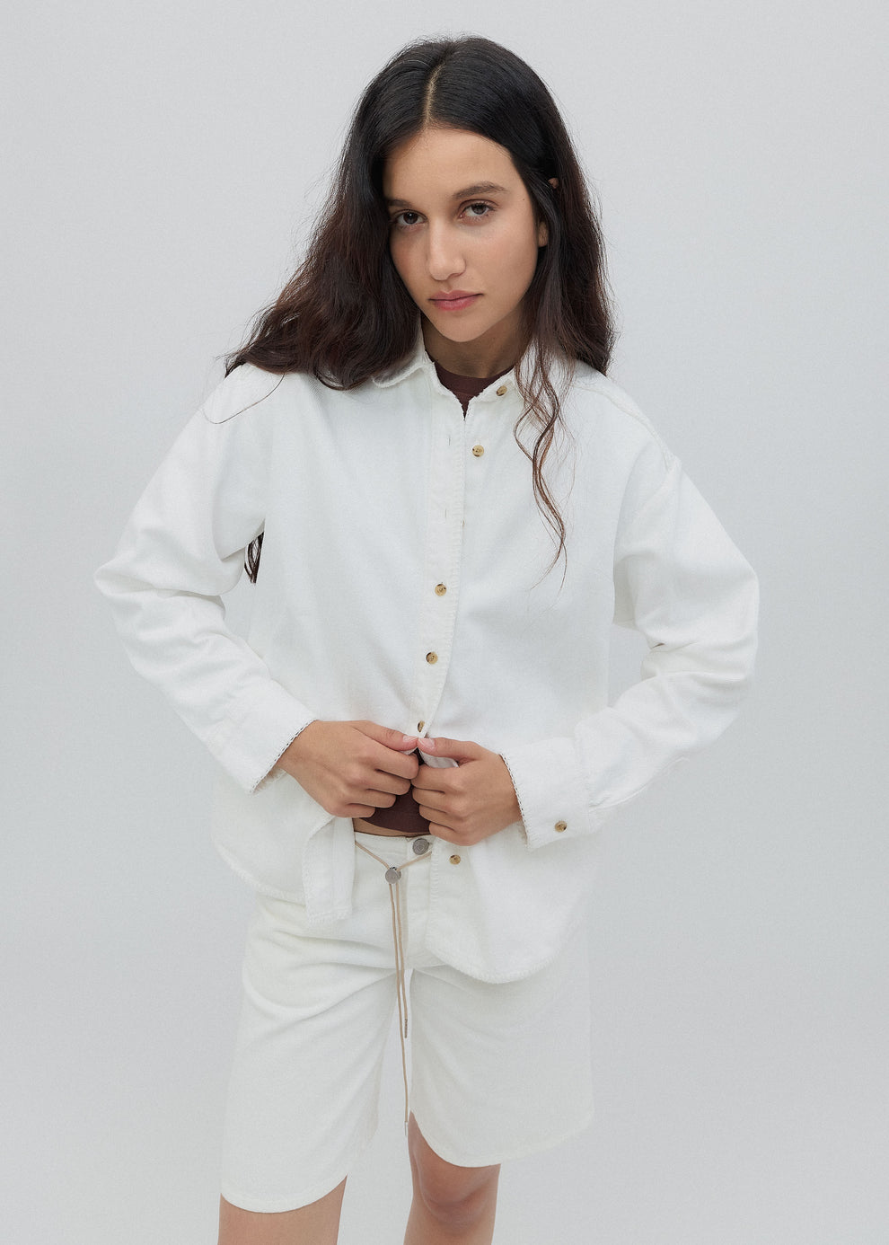 Woman wearing a white outfit with gold buttons on a plain background