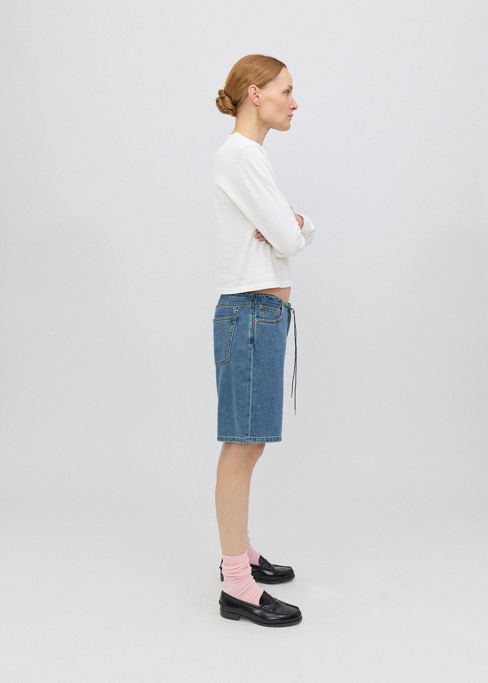 Woman wearing a white sweater and blue denim skirt on a plain background