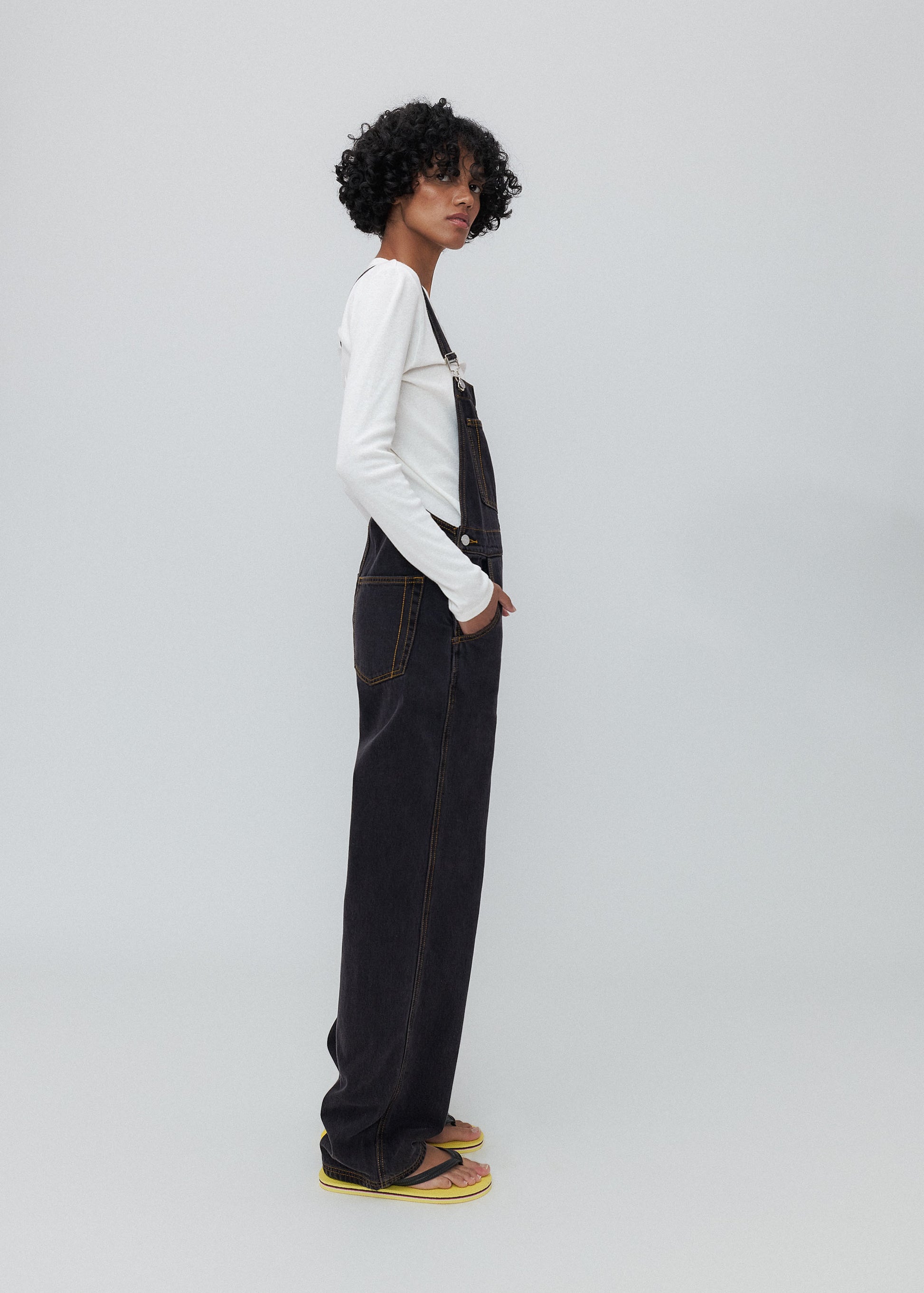 Person wearing black overalls and a white shirt on a light gray background