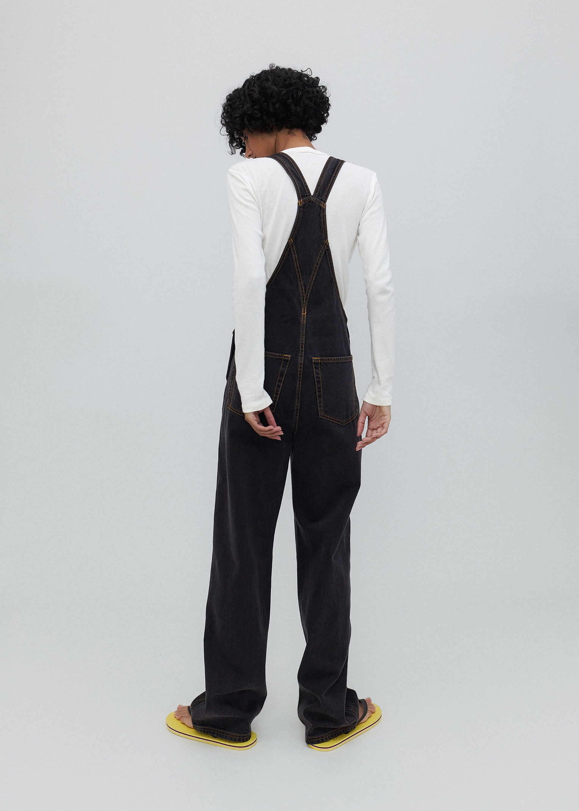 Person wearing black overalls and a white shirt on a plain background