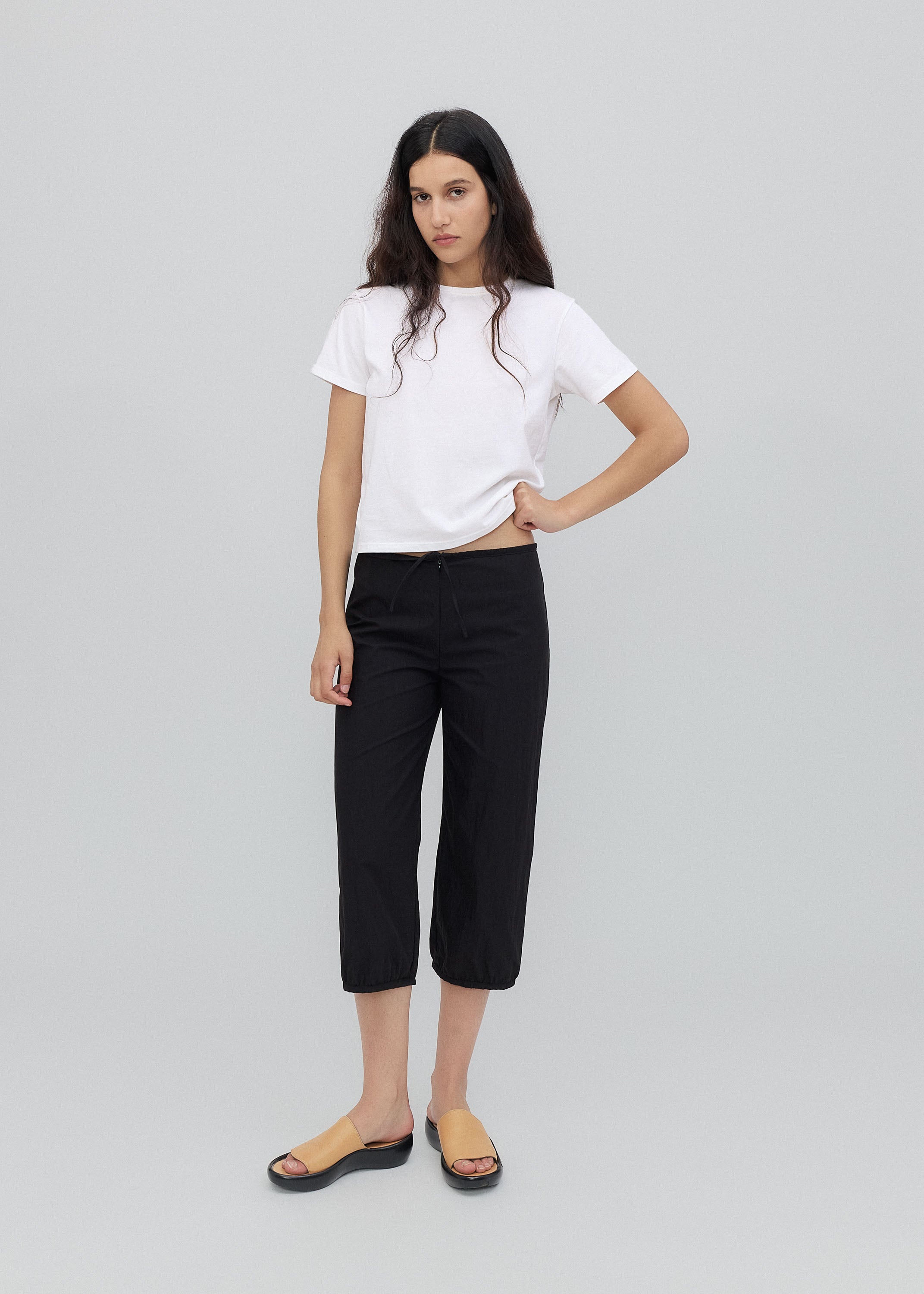 Woman wearing a white t-shirt and black pants on a light gray background