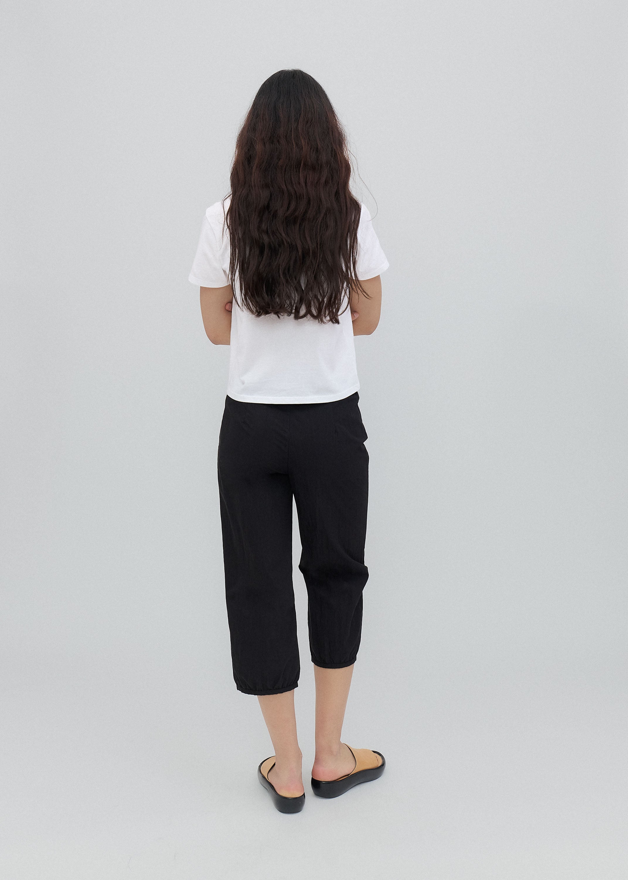 Person wearing a white shirt and black pants on a light gray background