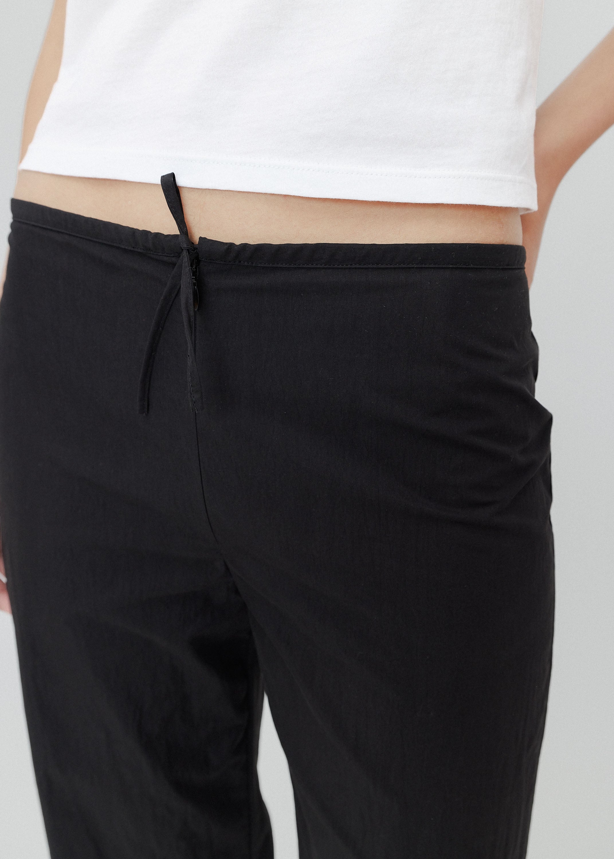 Black pants with a drawstring waist worn by a person on a light gray background