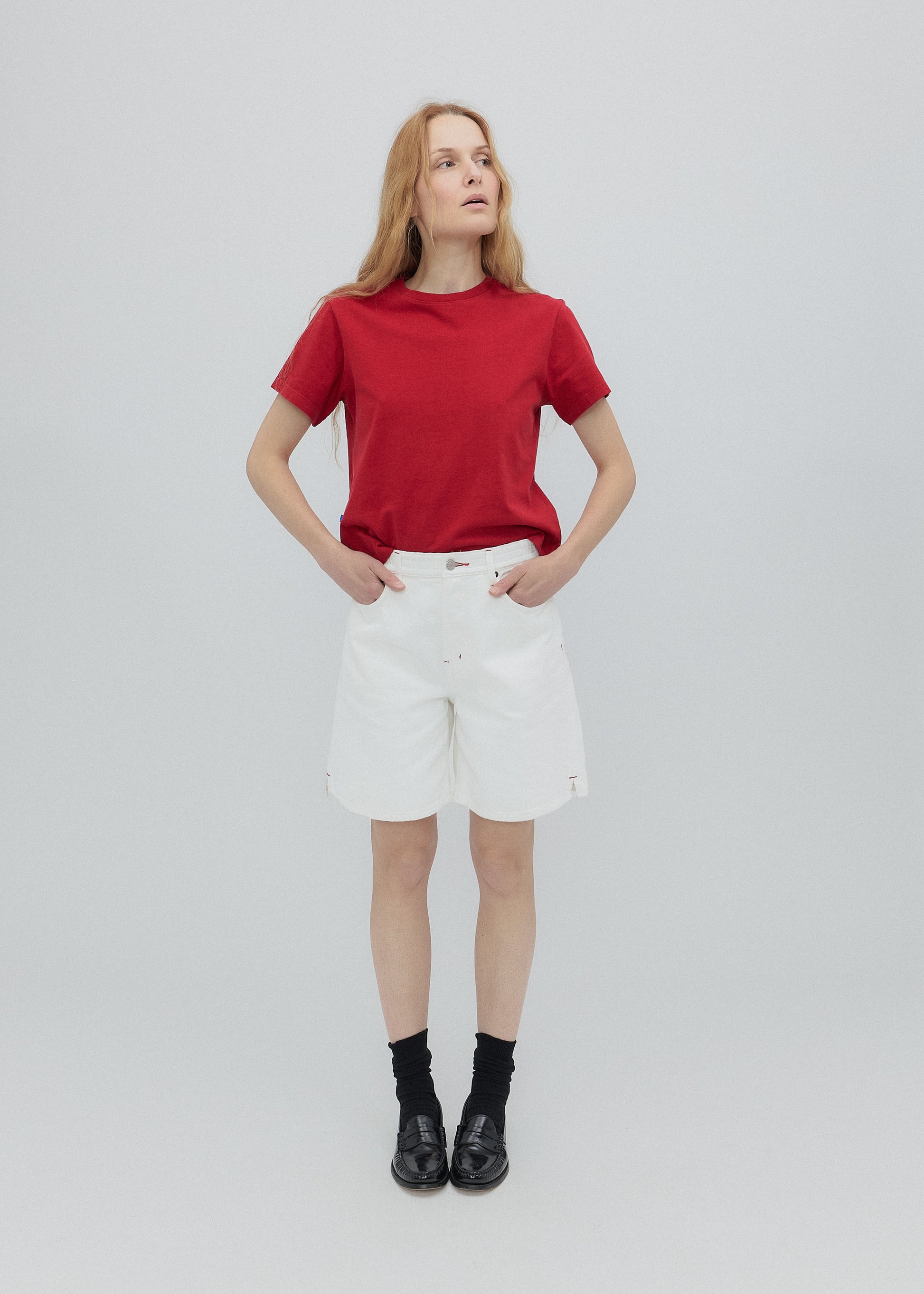 Person wearing a red t-shirt, white shorts, and black shoes on a light gray background